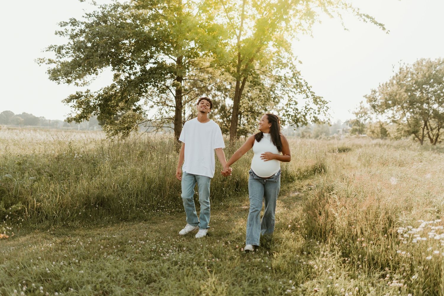 Two people walking together through a sunlit meadow with trees in the background.