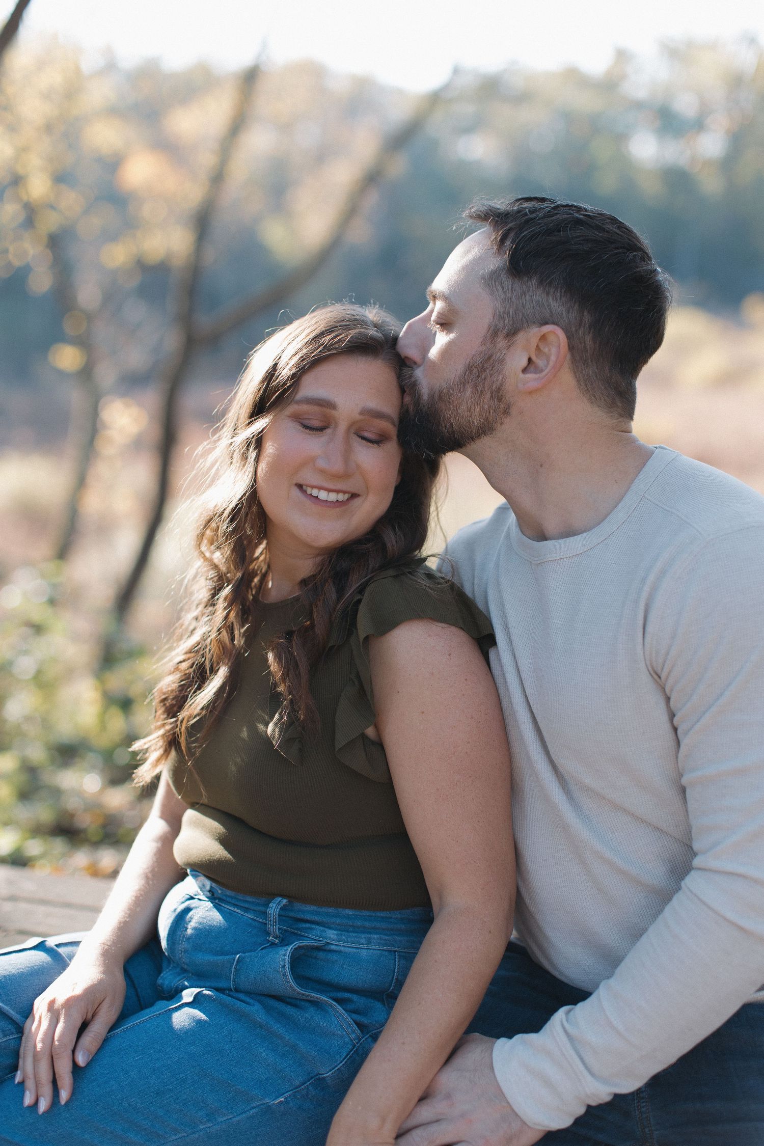 A playful couple sharing laughter while sitting outdoors in casual attire.