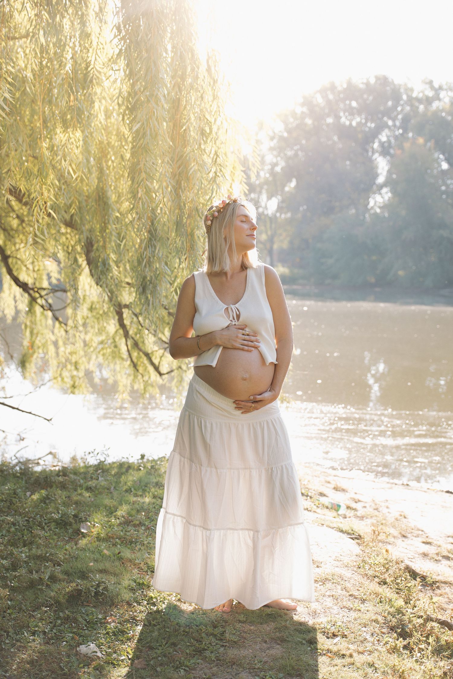 Ethereal maternity photos in white dress by a lake during golden hour.