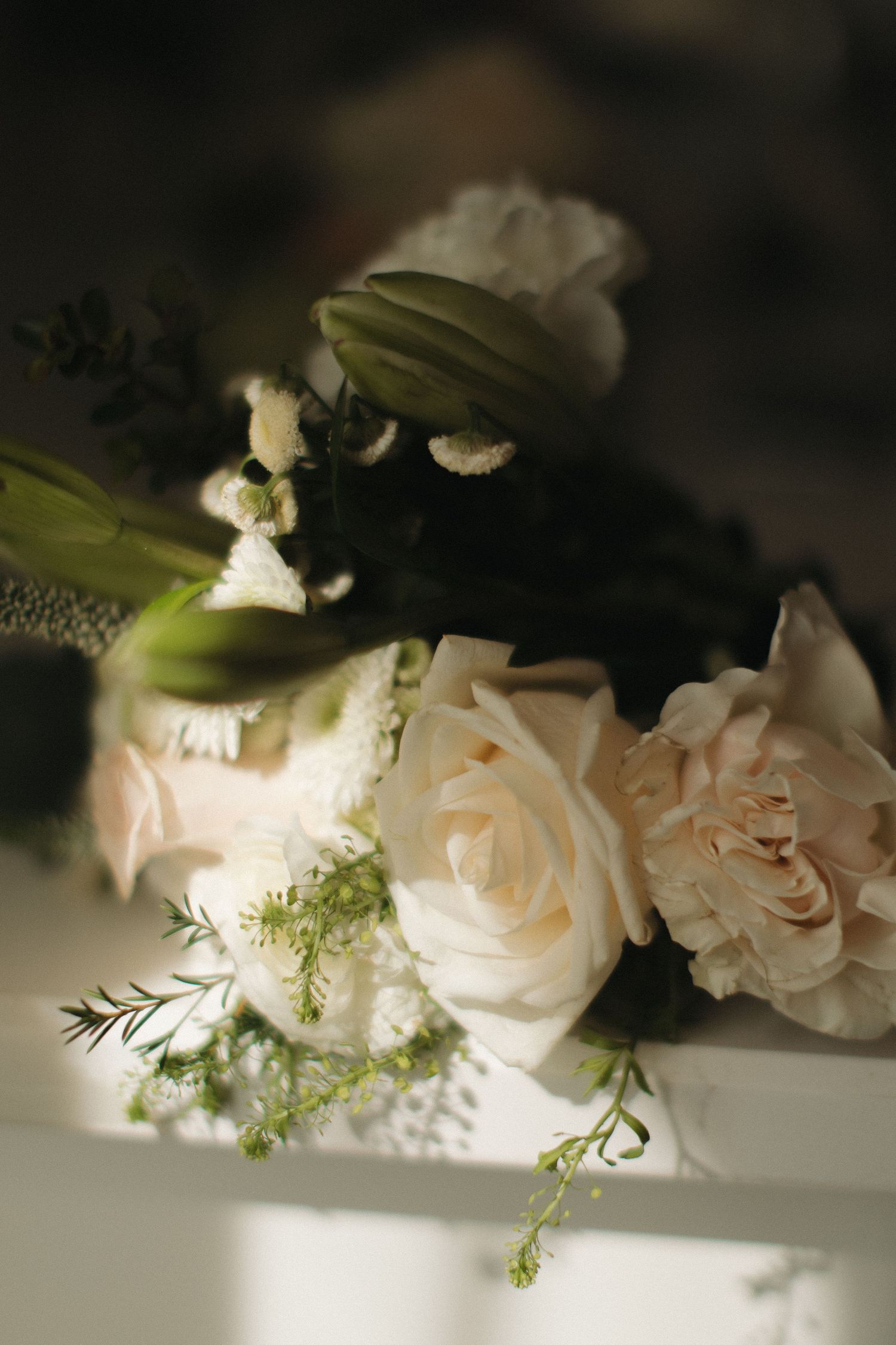 Elegant bridal bouquet with blush roses, white carnations, and green buds arranged in soft natural light.