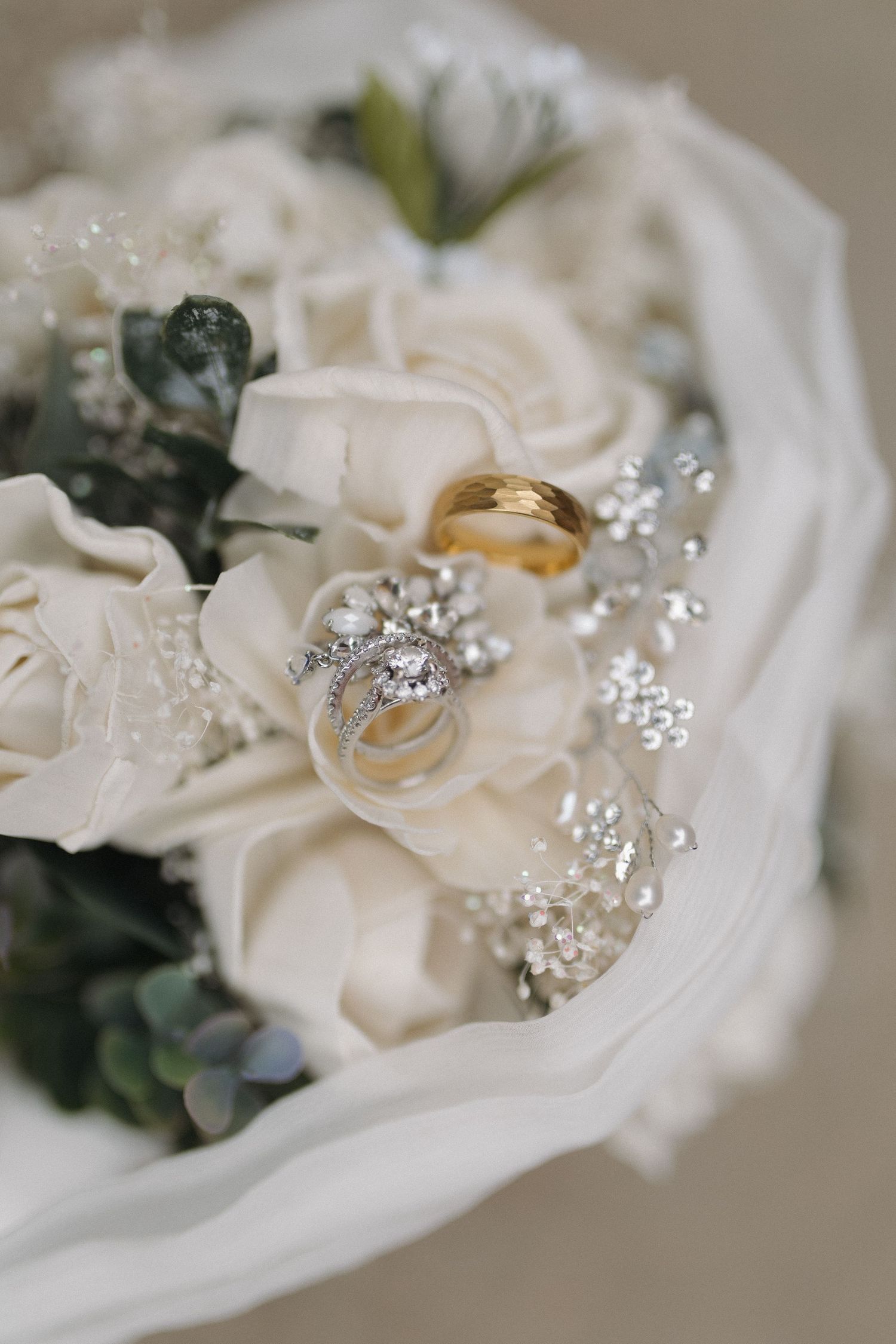 Wedding rings and jewelry arranged on white roses with sparkling crystal accents.