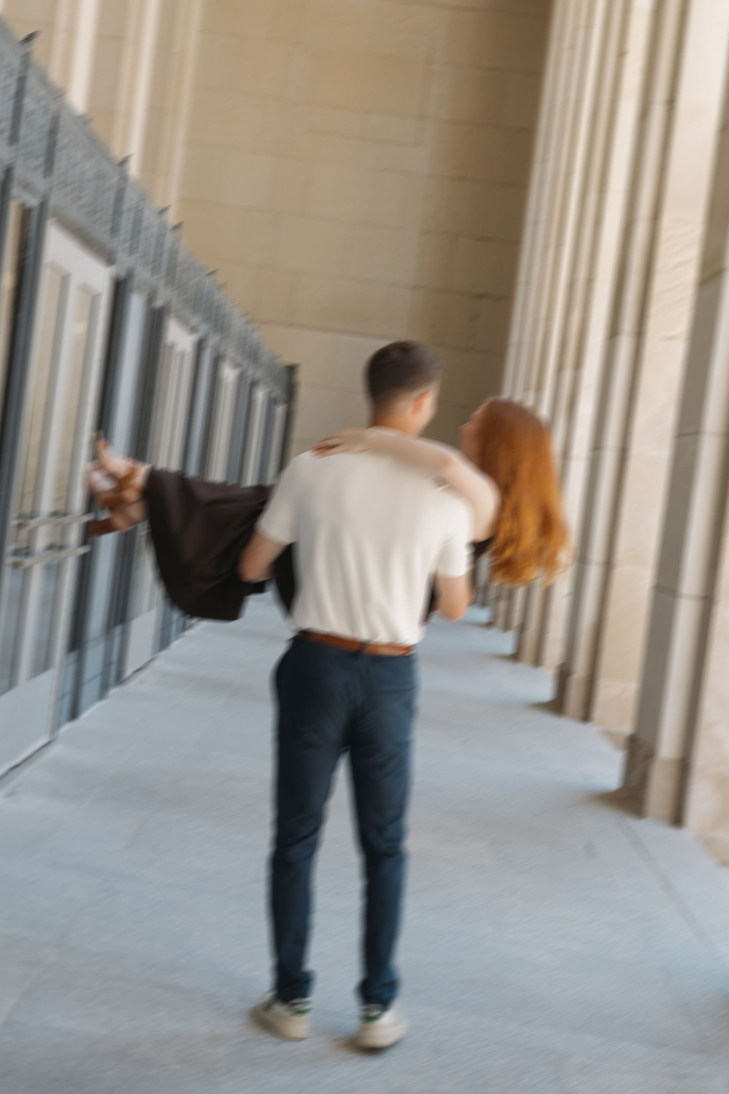 Couple walking together in a columned hallway, man in white shirt and jeans with arm around redhead woman.