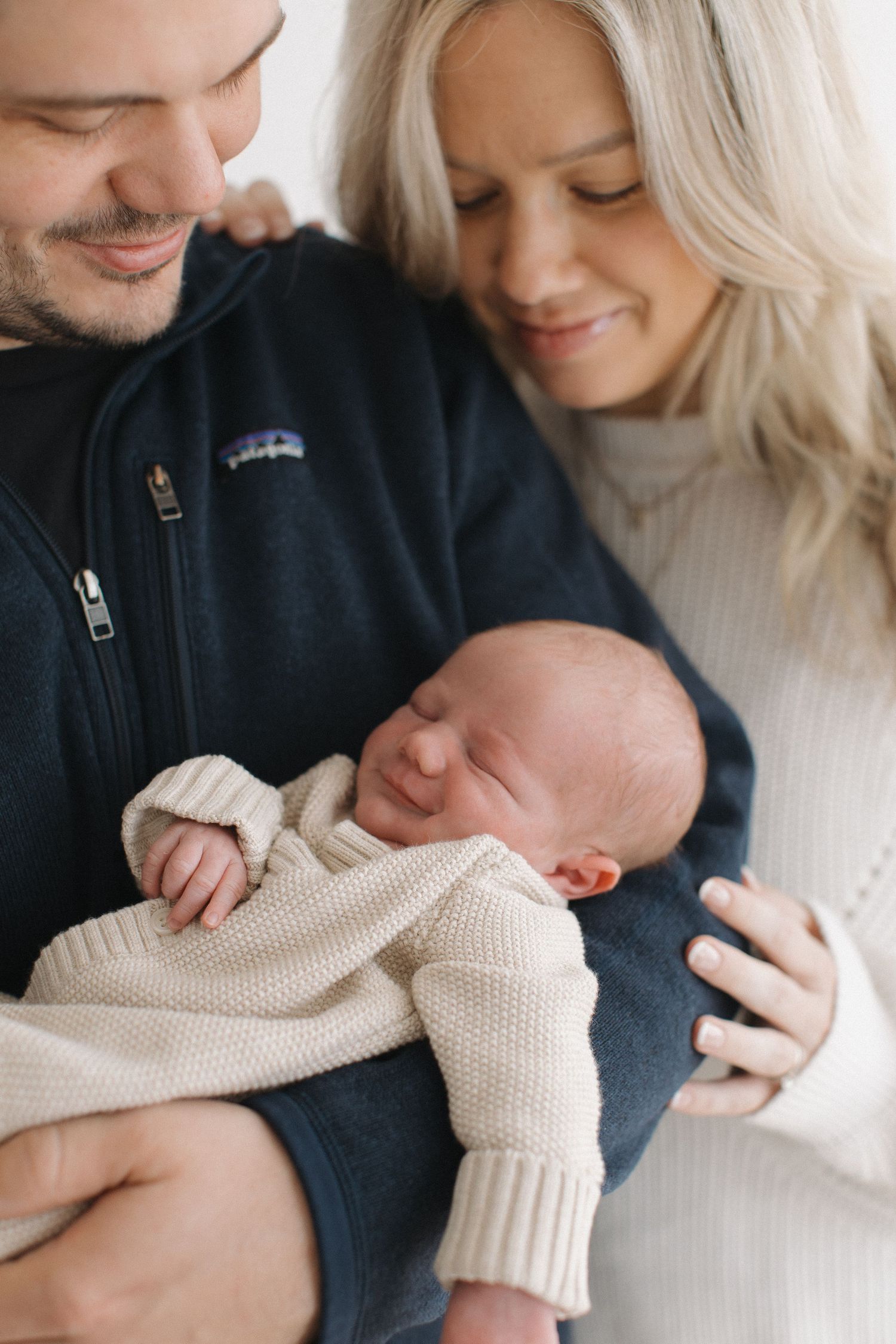 Tender newborn photography session showing parents cradling baby wrapped in cream knit blanket.