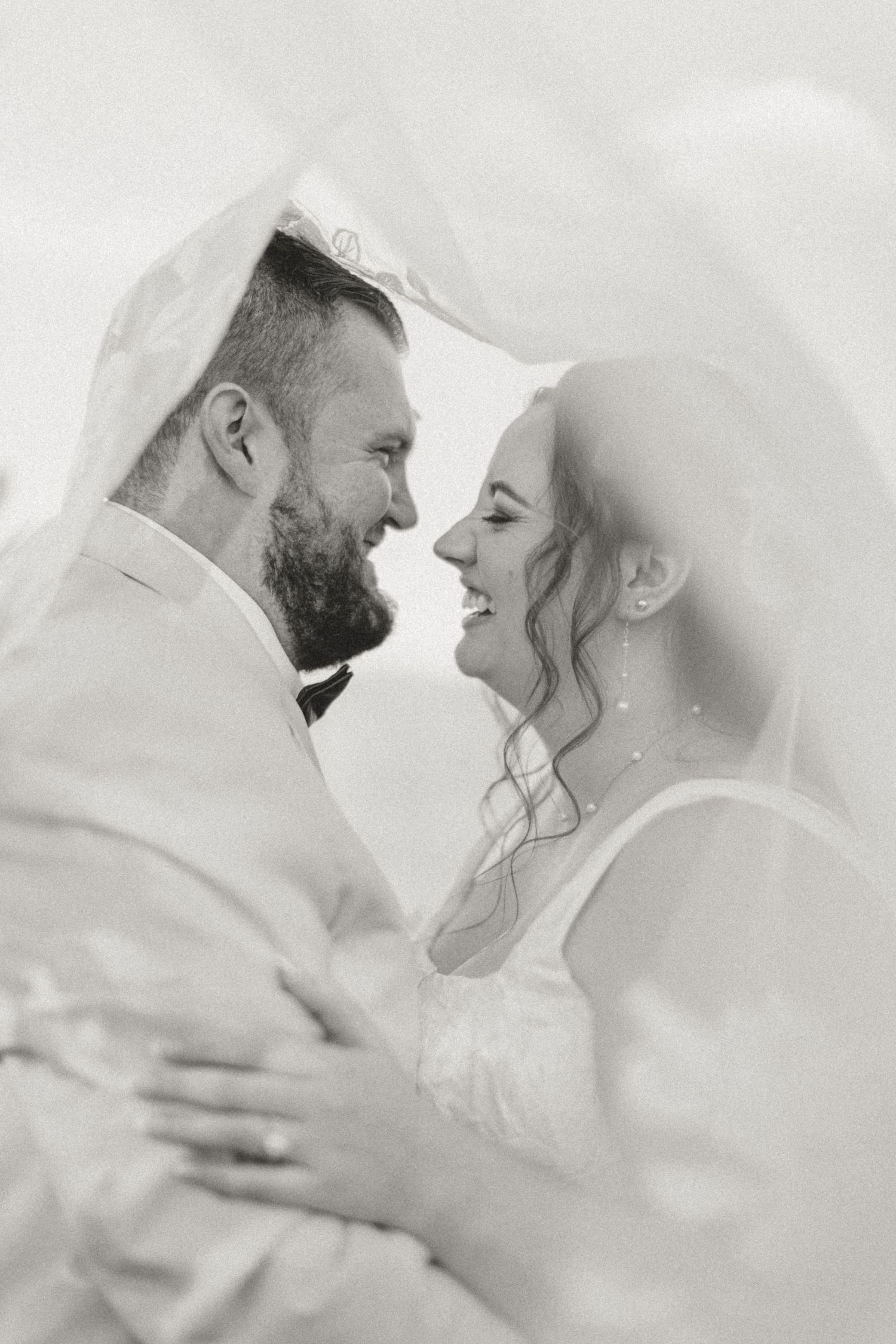 Romantic black and white portrait of newlyweds under veil.