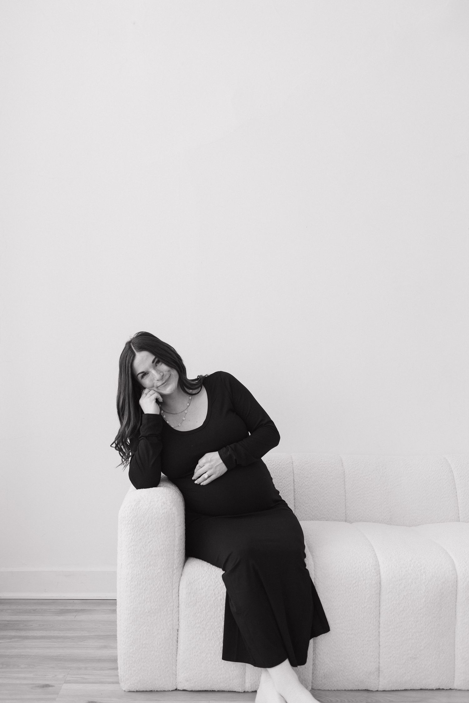 A minimalist maternity portrait with a person in black resting on a white couch.
