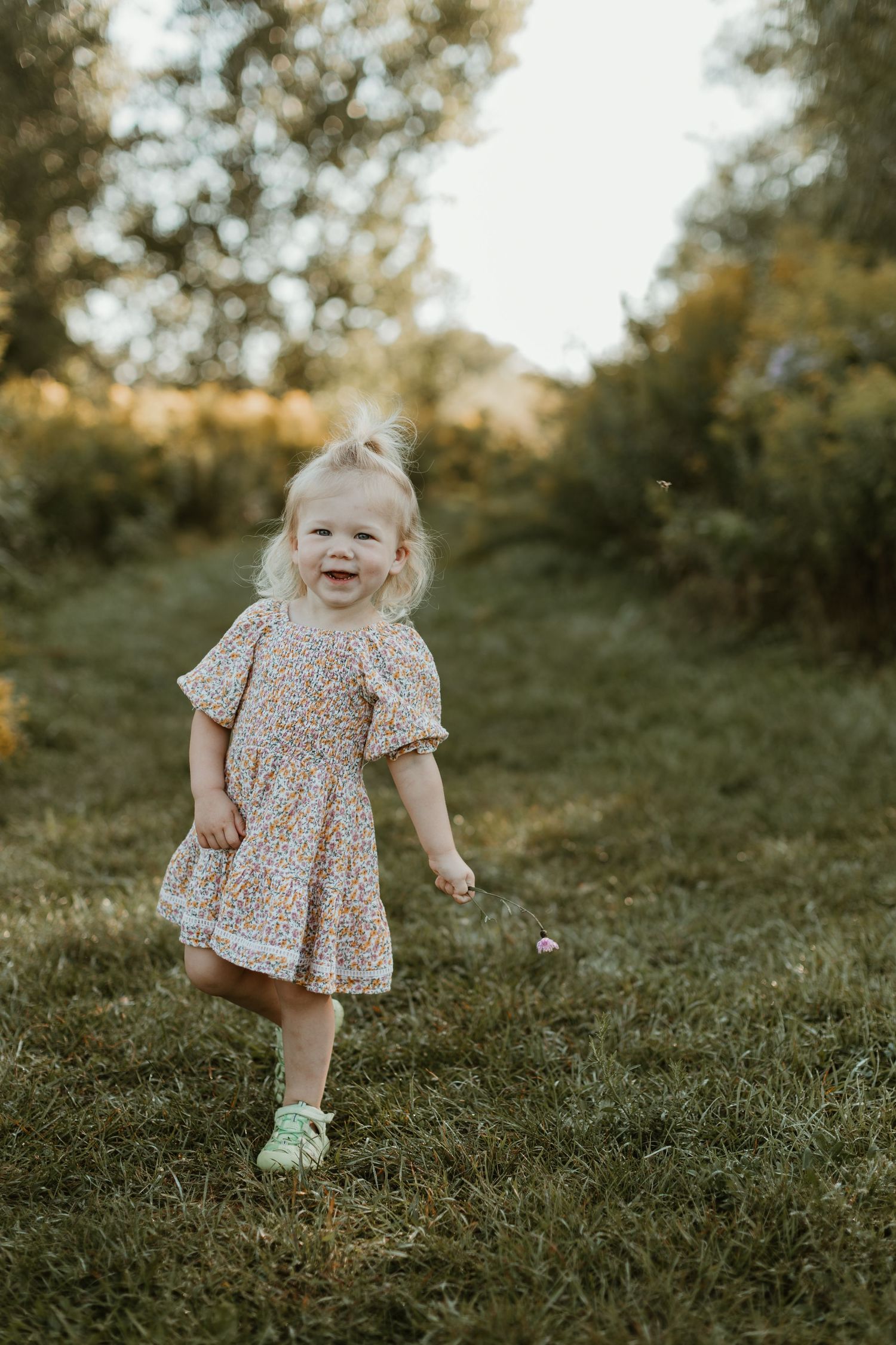 Toddler in floral dress running and playing on grassy hill at sunset.