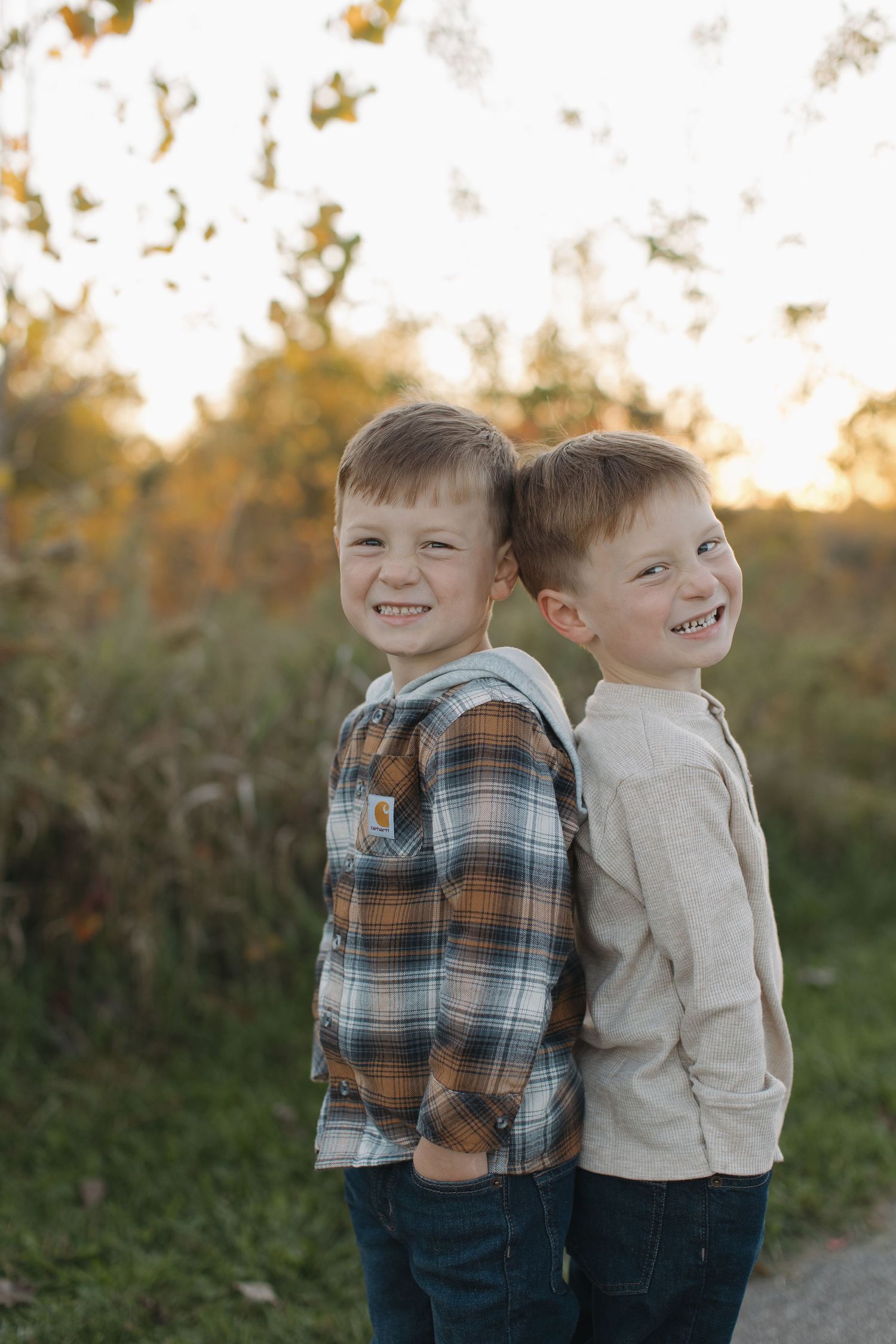 Two young children in casual clothing laughing together outdoors at sunset.