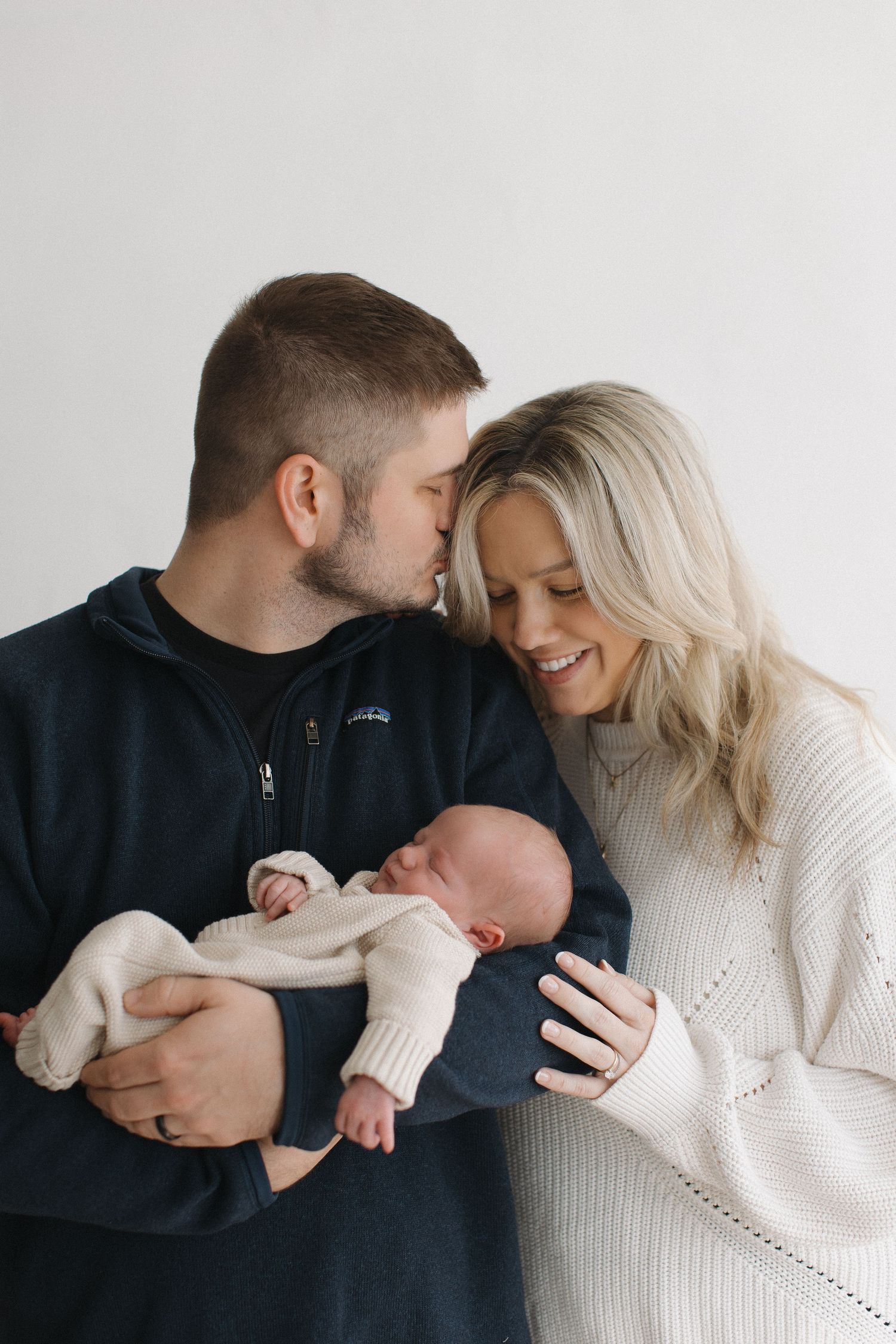 Tender family moment captured in white sweaters against neutral background.