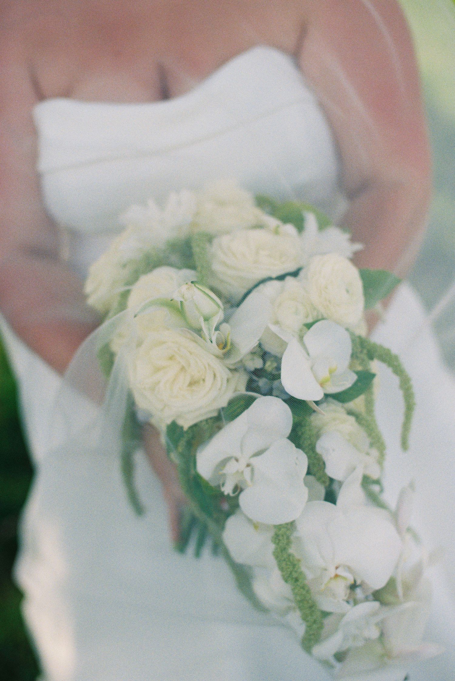 Bride holding a cascading white wedding bouquet with roses, orchids, and greenery against her white strapless gown.