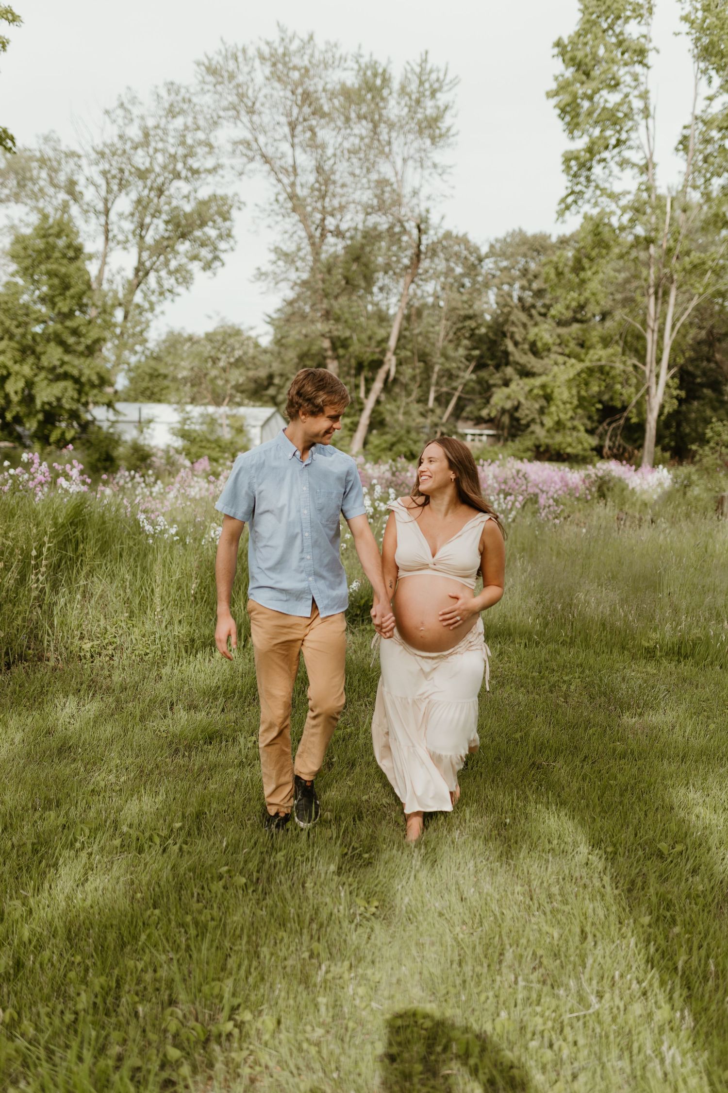A couple strolls through tall grass during their outdoor maternity photo session.