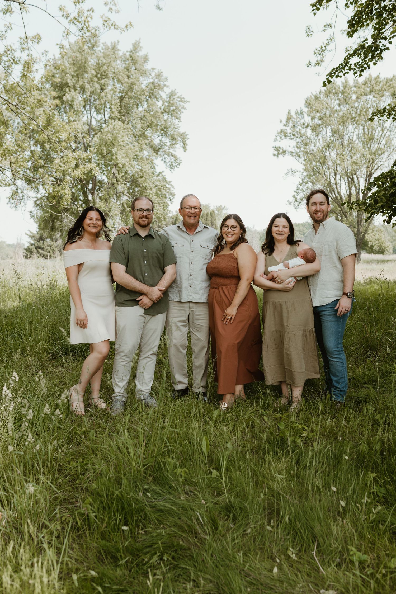 Extended family group posing together in tall grass during an outdoor photo shoot.
