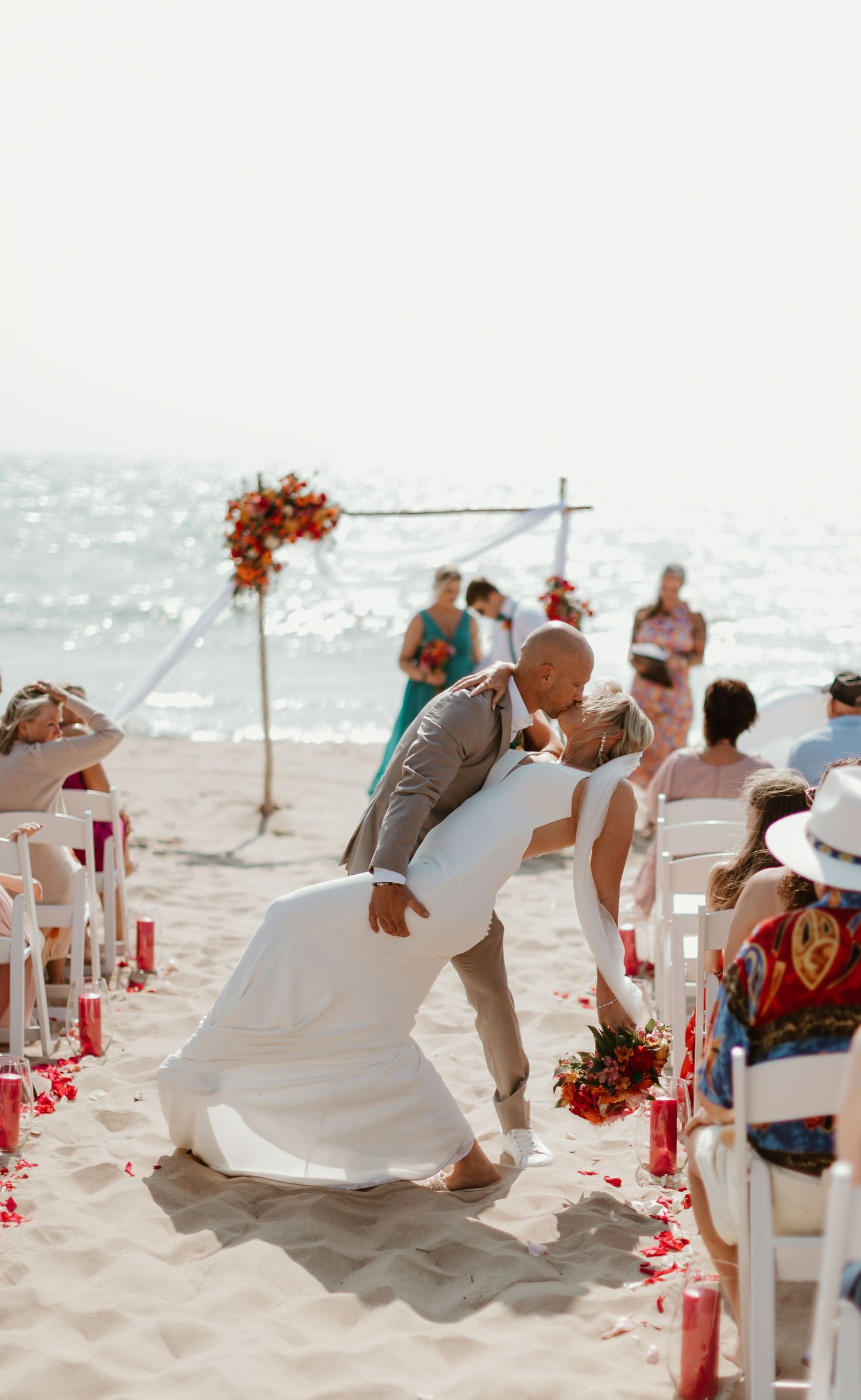 Beach wedding ceremony with white chairs and coral floral arch by the ocean.