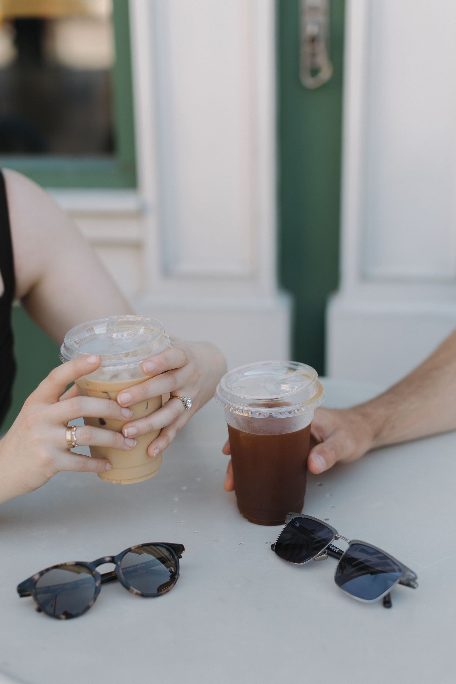 Two people toasting with iced coffee drinks on a white table with sunglasses nearby.