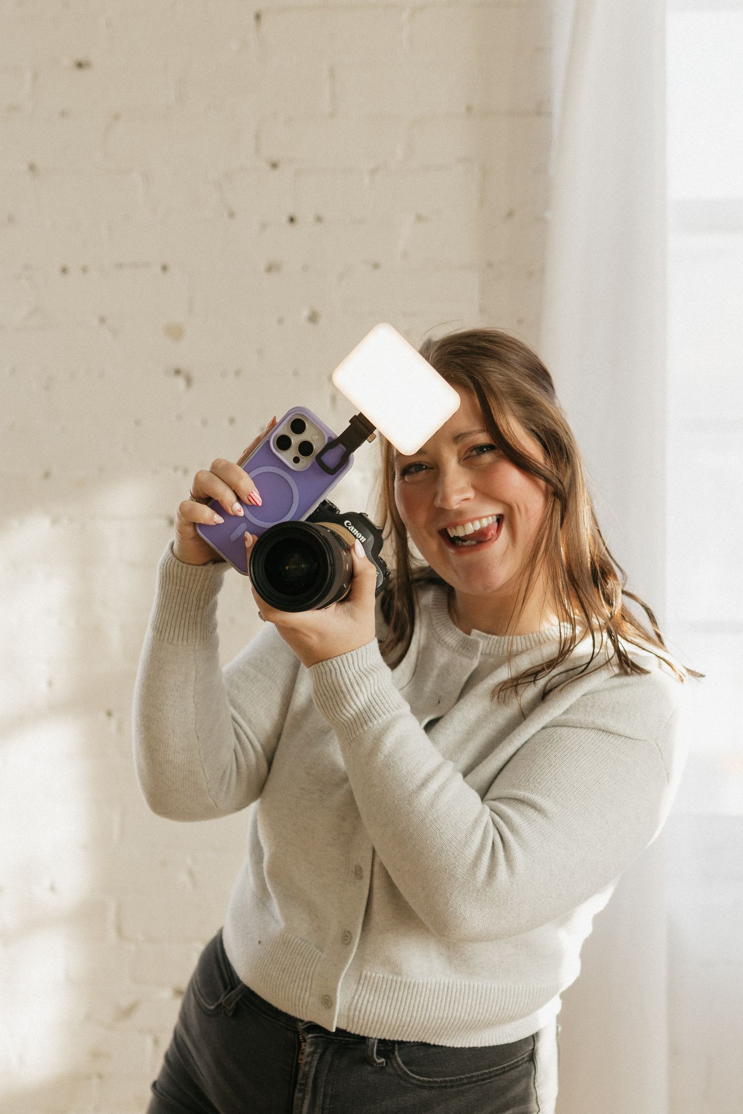 Photographer in cream sweater taking selfies in bright studio.