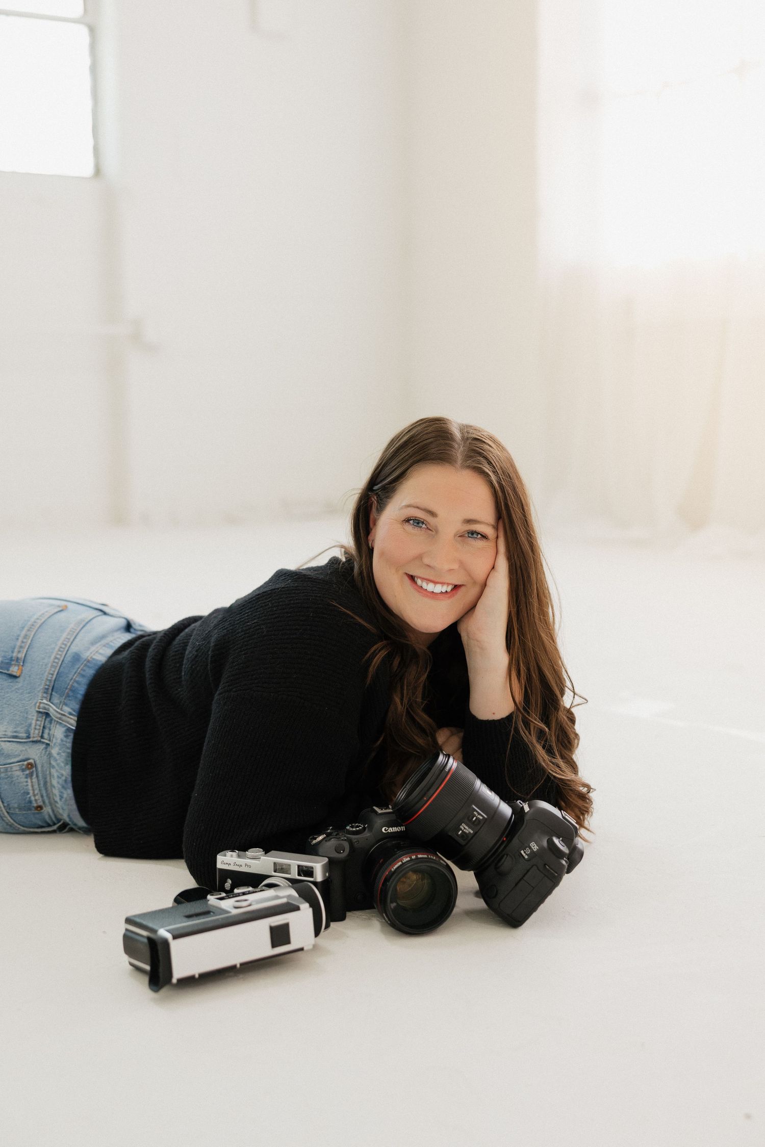 Professional photographer lying on floor with camera equipment in bright studio setting.