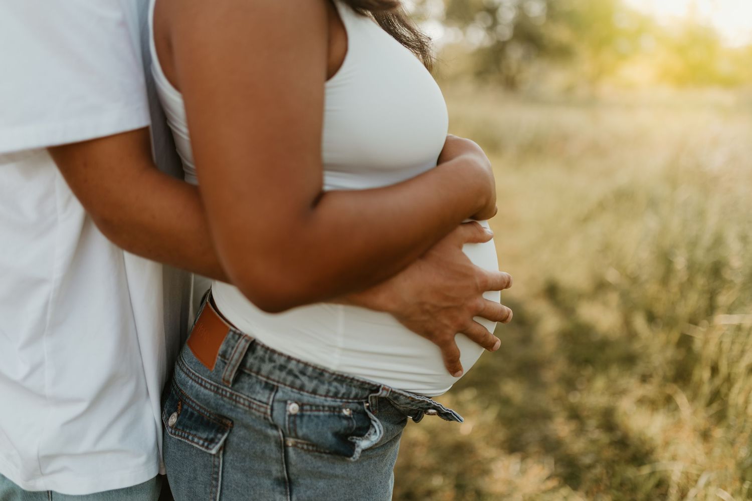 Two people embrace in casual white tops and jeans during golden hour.