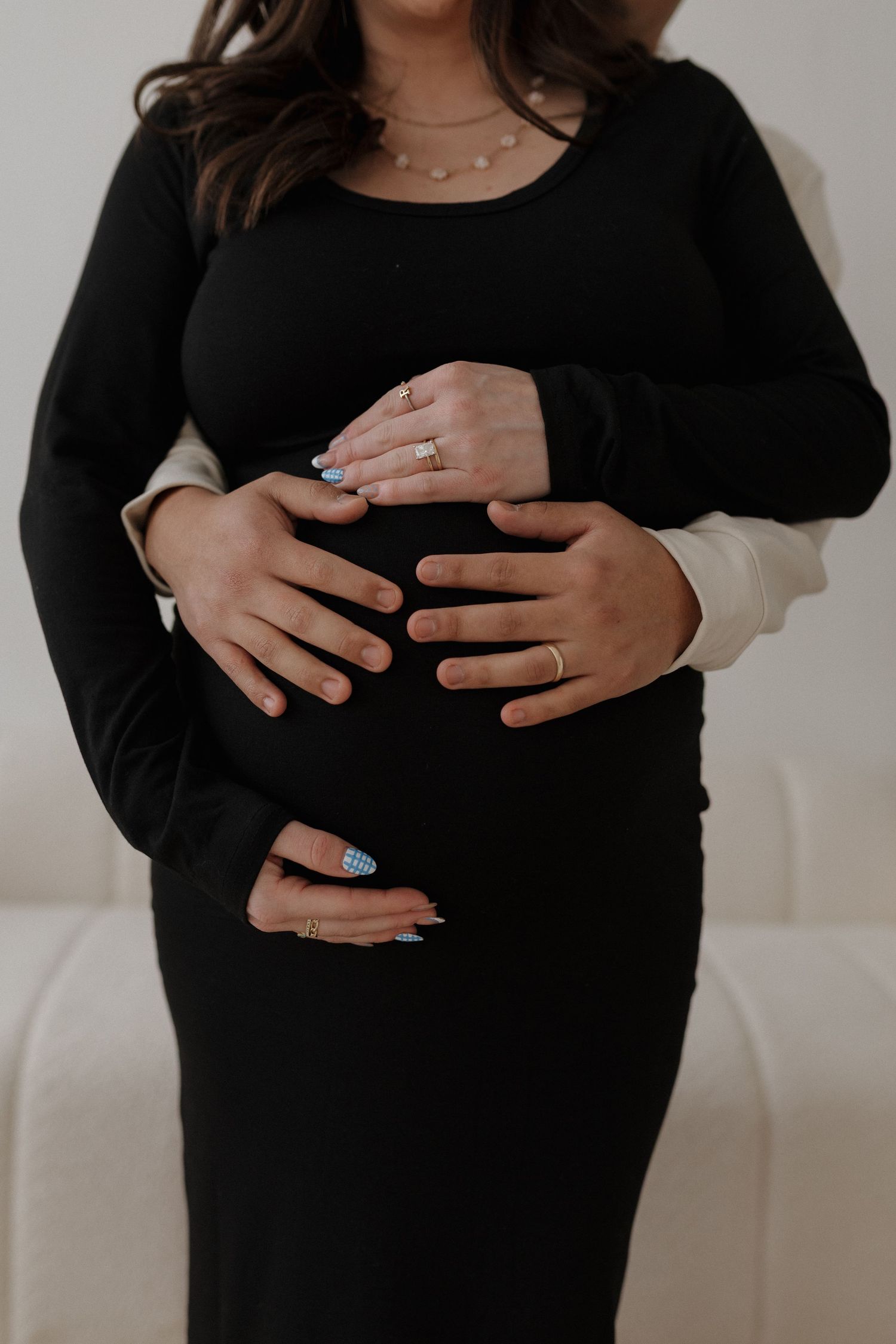 Close-up shots of hands cradling a pregnant belly in a black dress.