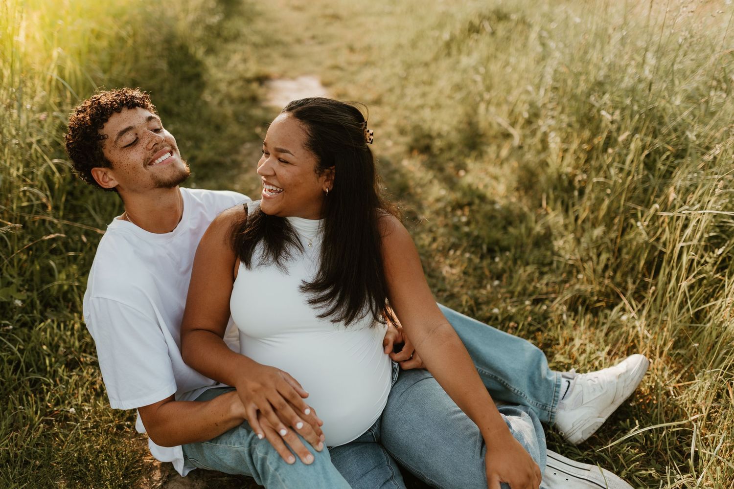 Couple laughing together while laying in tall grass during sunset.
