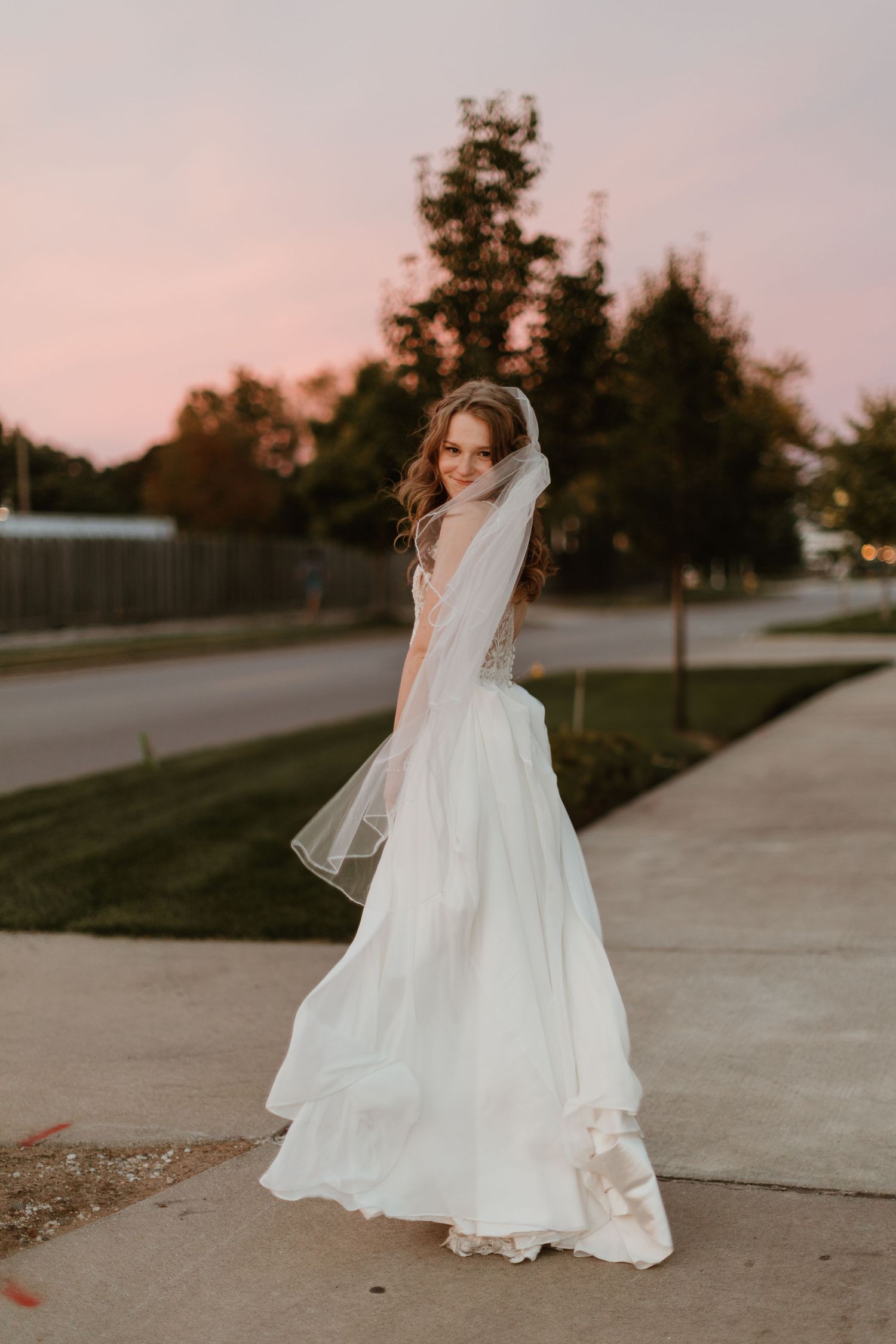 Bride twirling in flowing wedding dress and veil during sunset photo session.