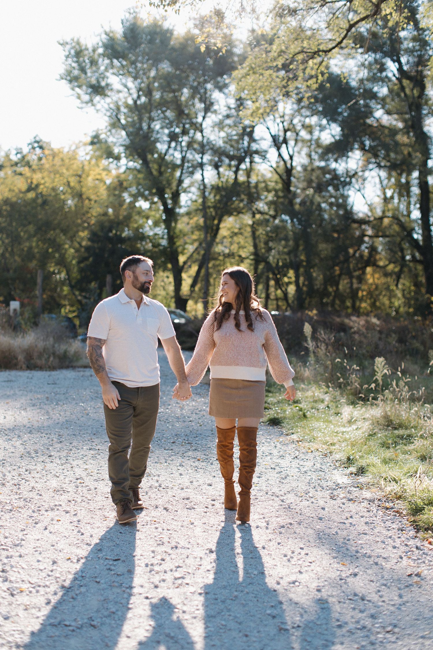 A couple walking hand in hand on a sunlit gravel path.