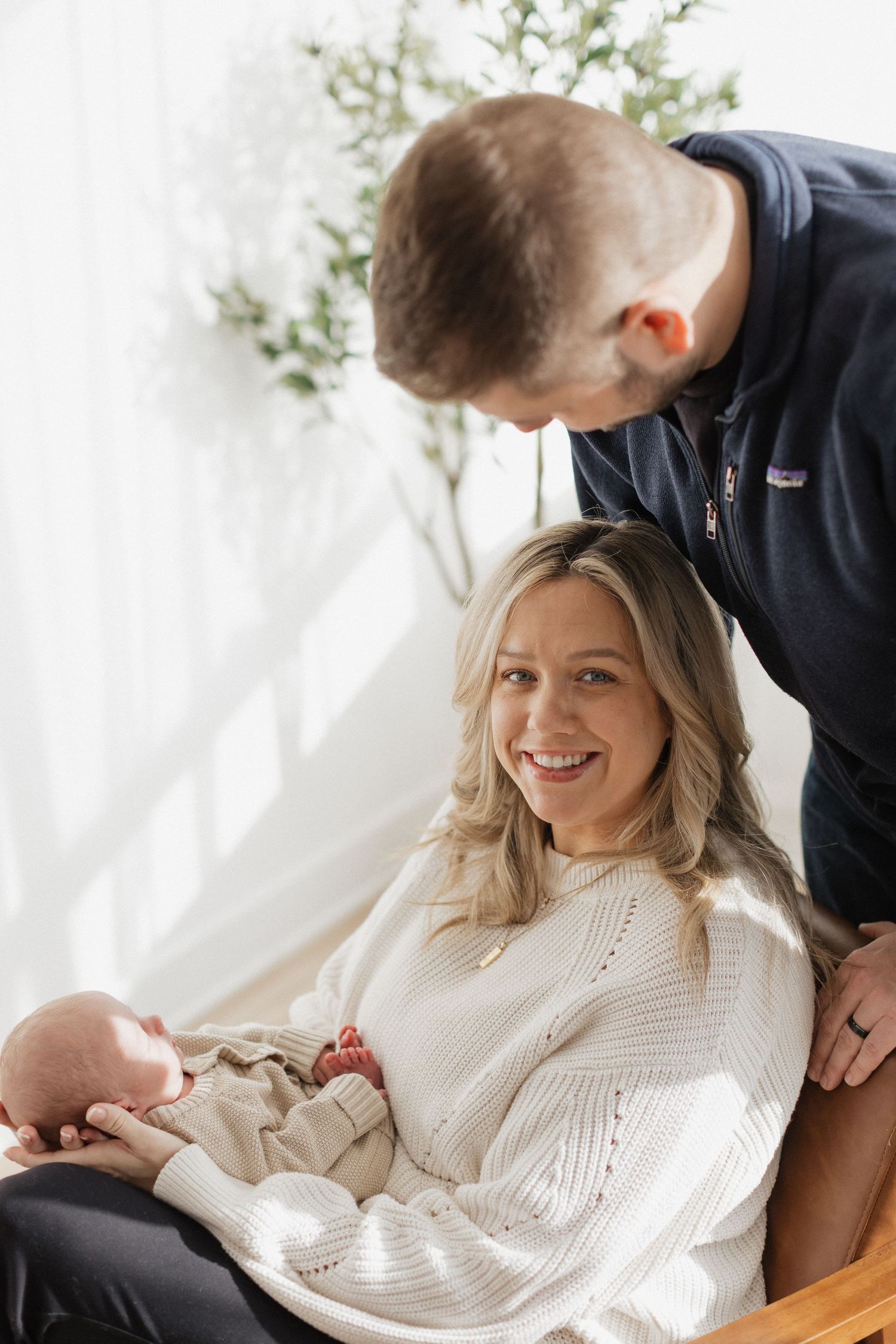 A couple in casual attire shares loving glances during an indoor photoshoot with white backdrop.