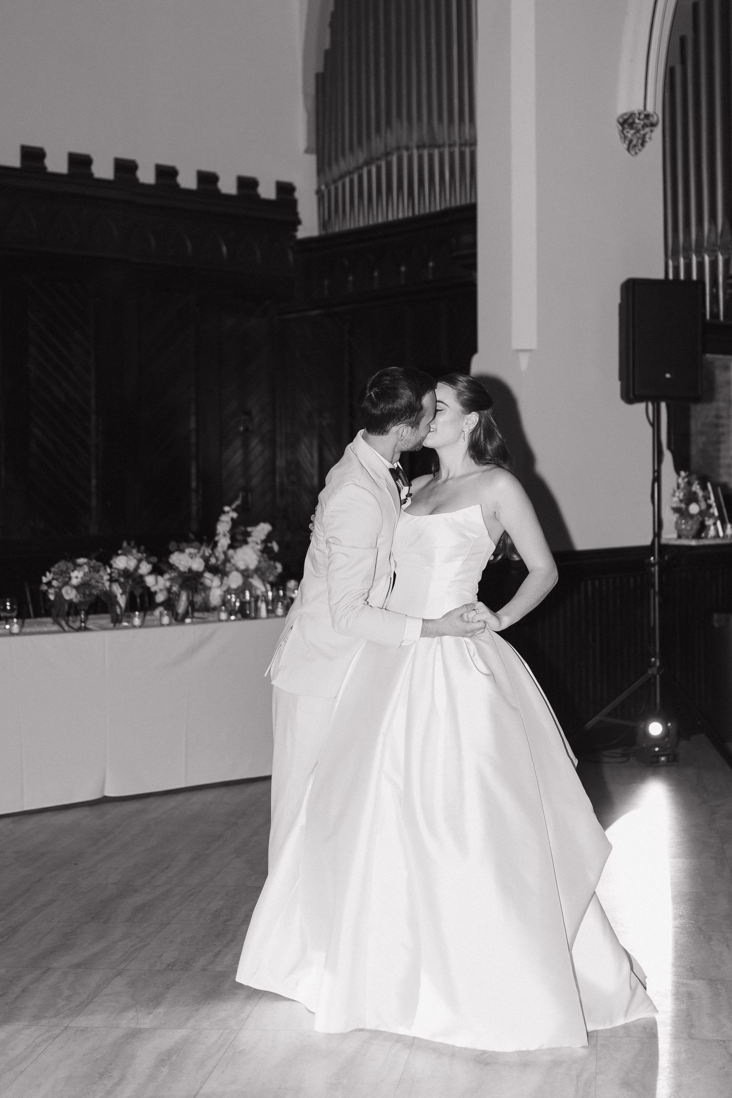 A couple shares their first dance in an elegant ballroom with dramatic lighting.