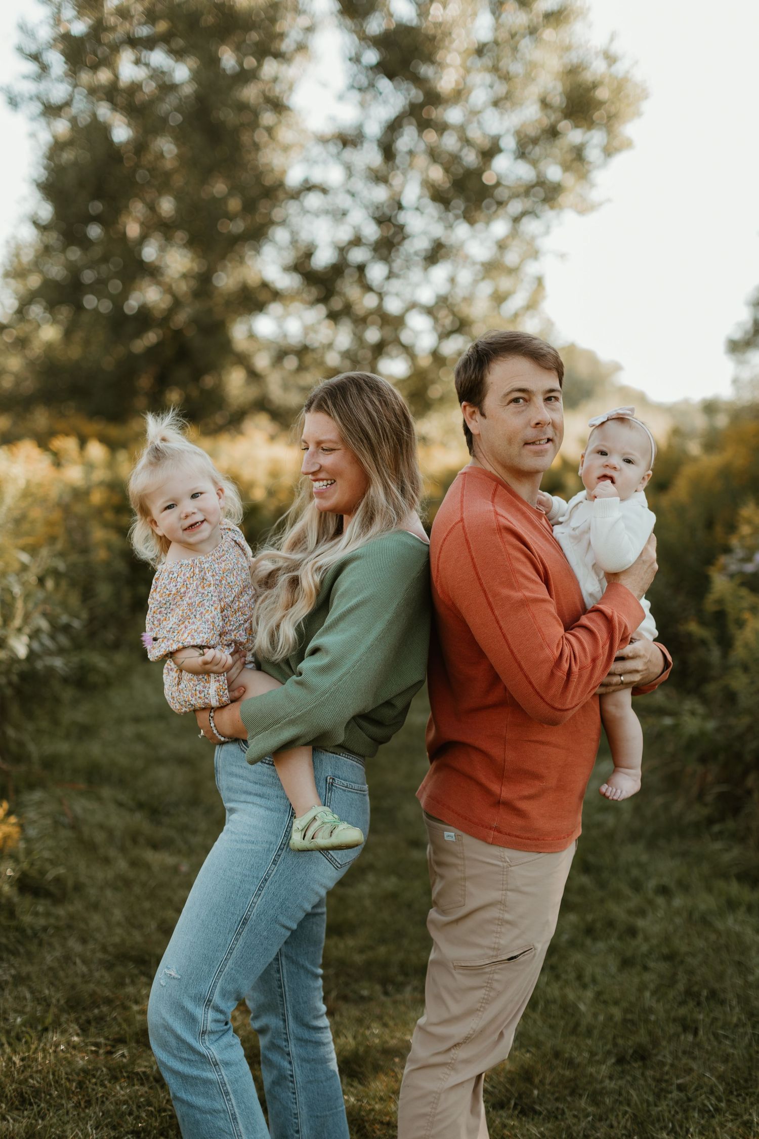 Joyful family moment captured outdoors with parents holding children against natural backdrop.