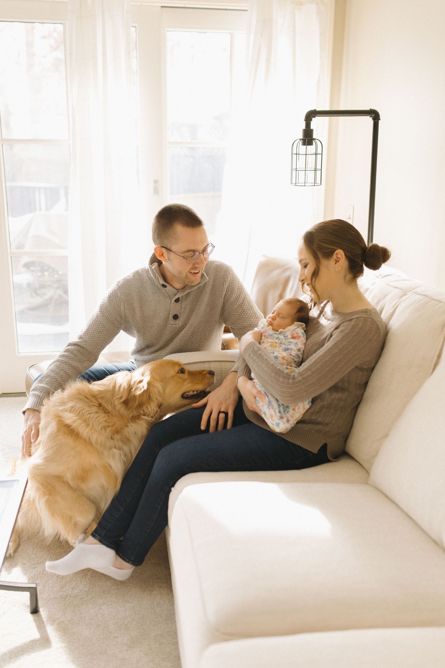 Couple relaxing on white couch with golden retriever in bright sunlit room.