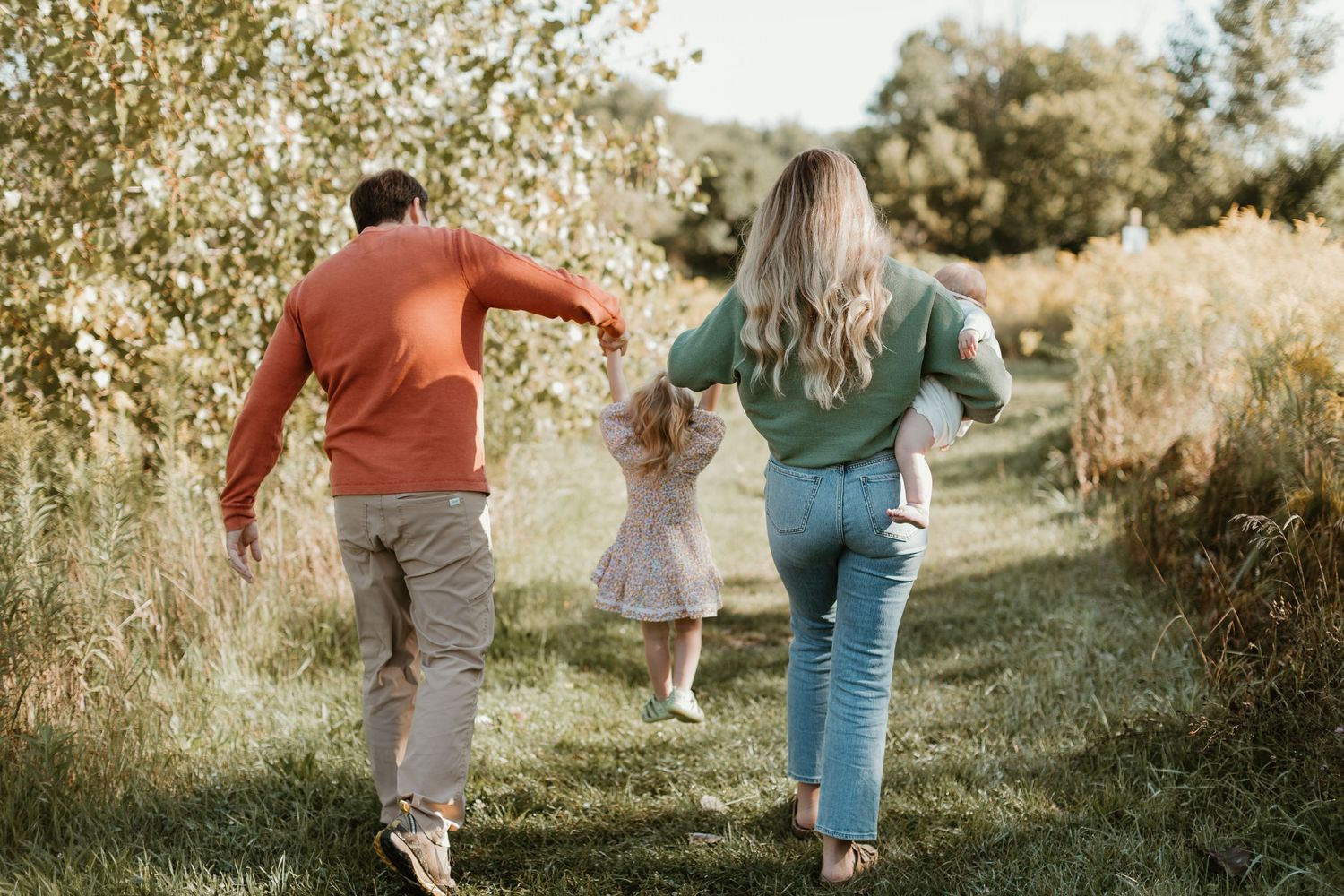 Family walking and playing together on grassy hill during sunset photoshoot.