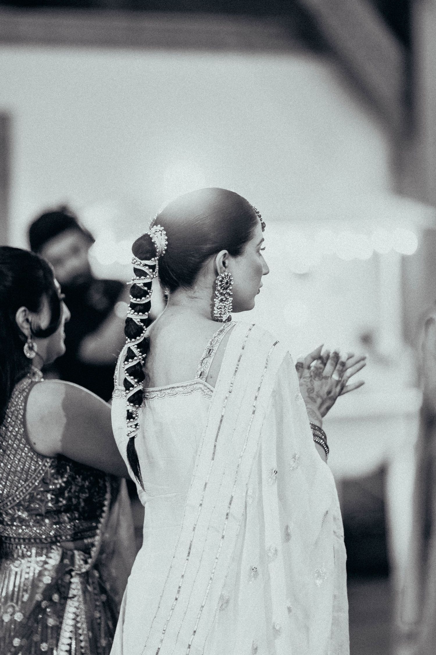 Traditional Indian wedding hairstyle with jasmine flowers woven into long braid, wearing white sari with delicate details.