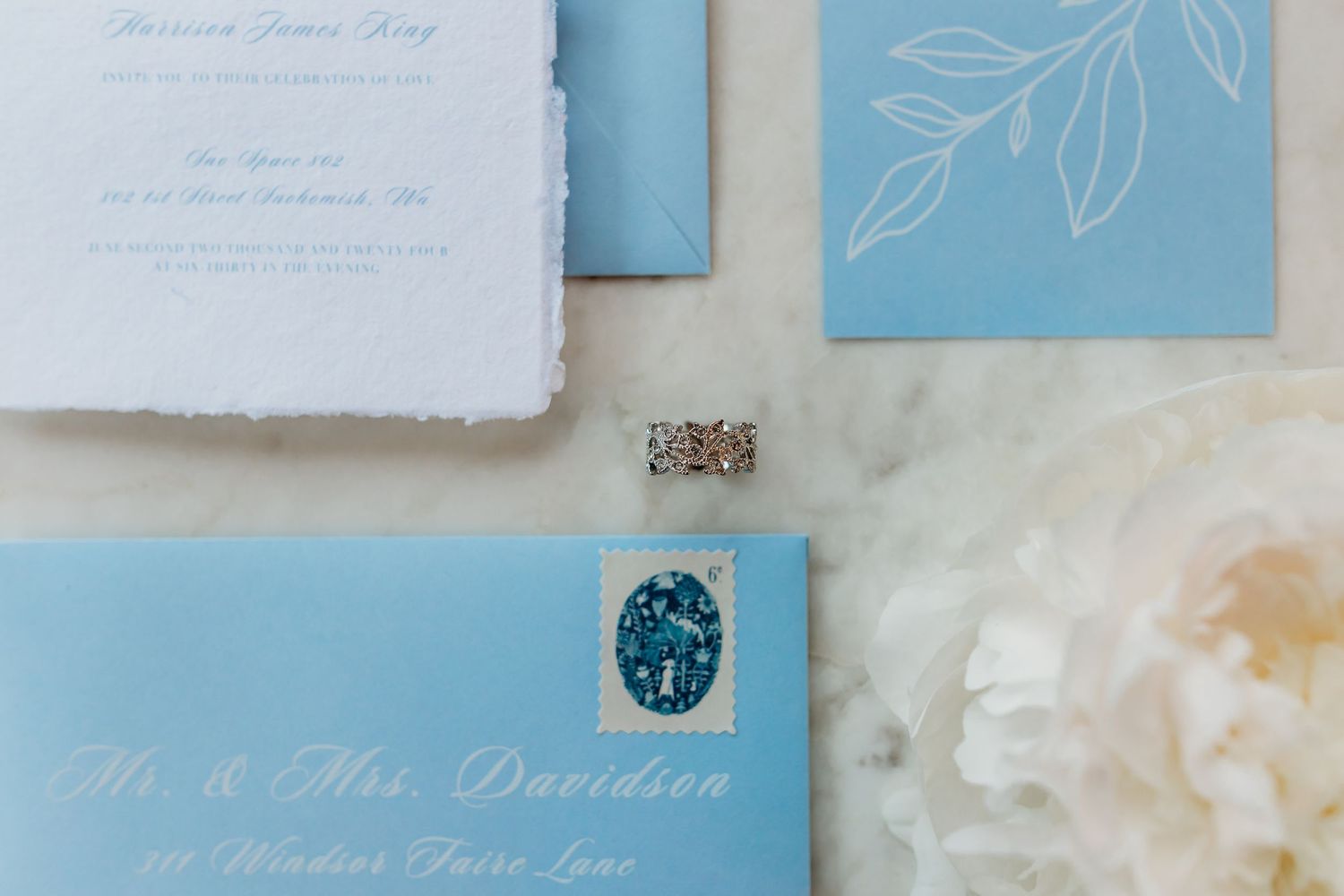 Light blue wedding stationery with calligraphy and floral designs on marble.