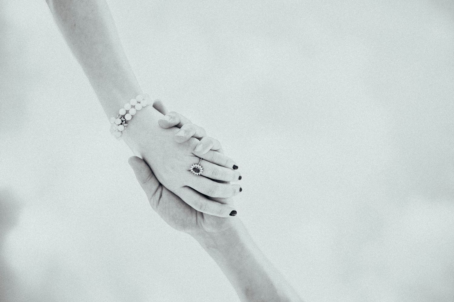 Elegant black and white close-up of bride and groom holding hands with pearl bracelet and ring.