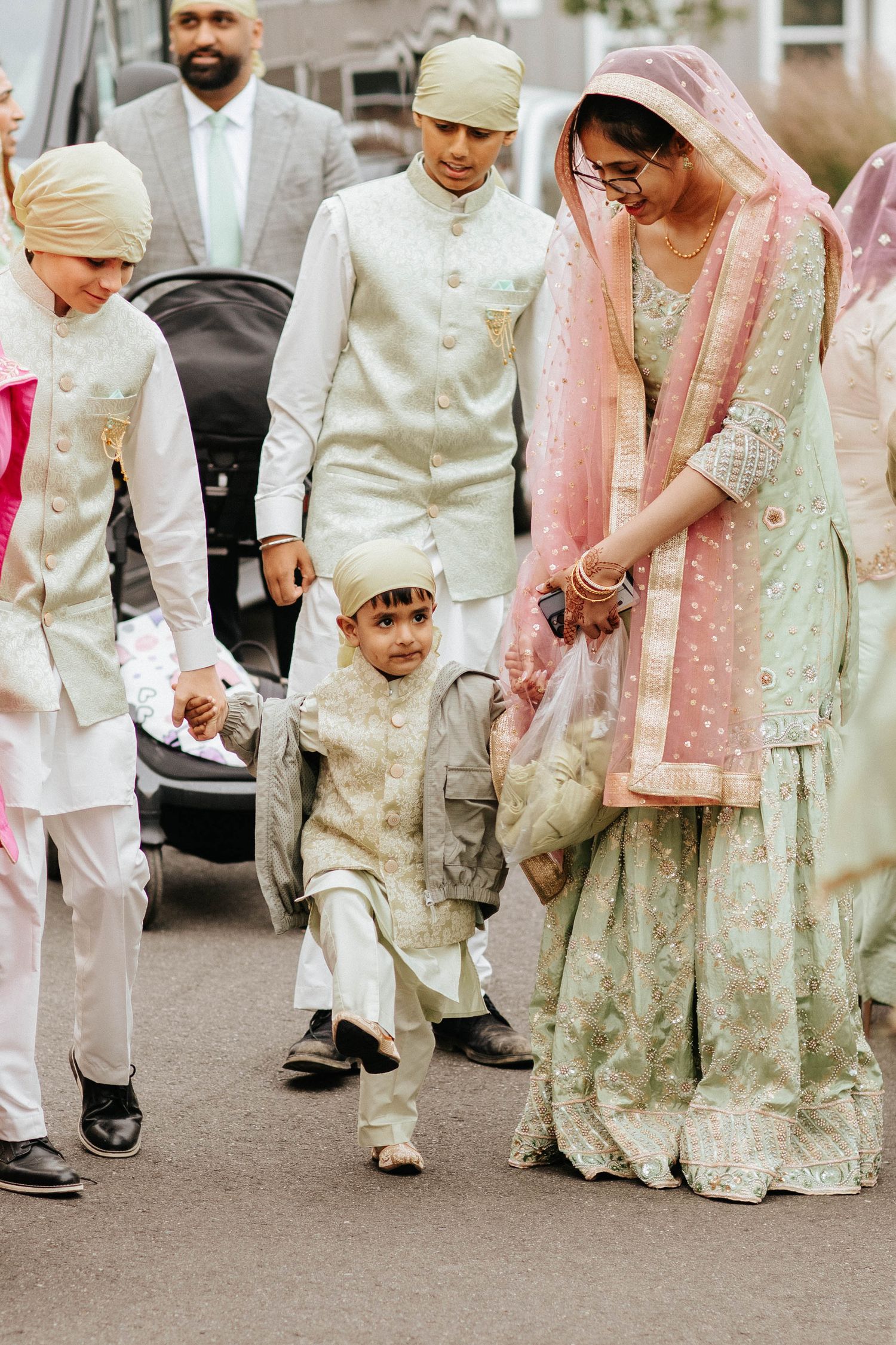 A traditional South Asian wedding party wearing elegant cream and pastel colored formal attire walking together outdoors.
