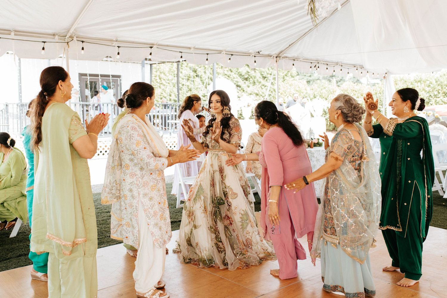 Wedding guests gather under a white tent canopy, dancing and celebrating at an outdoor reception.