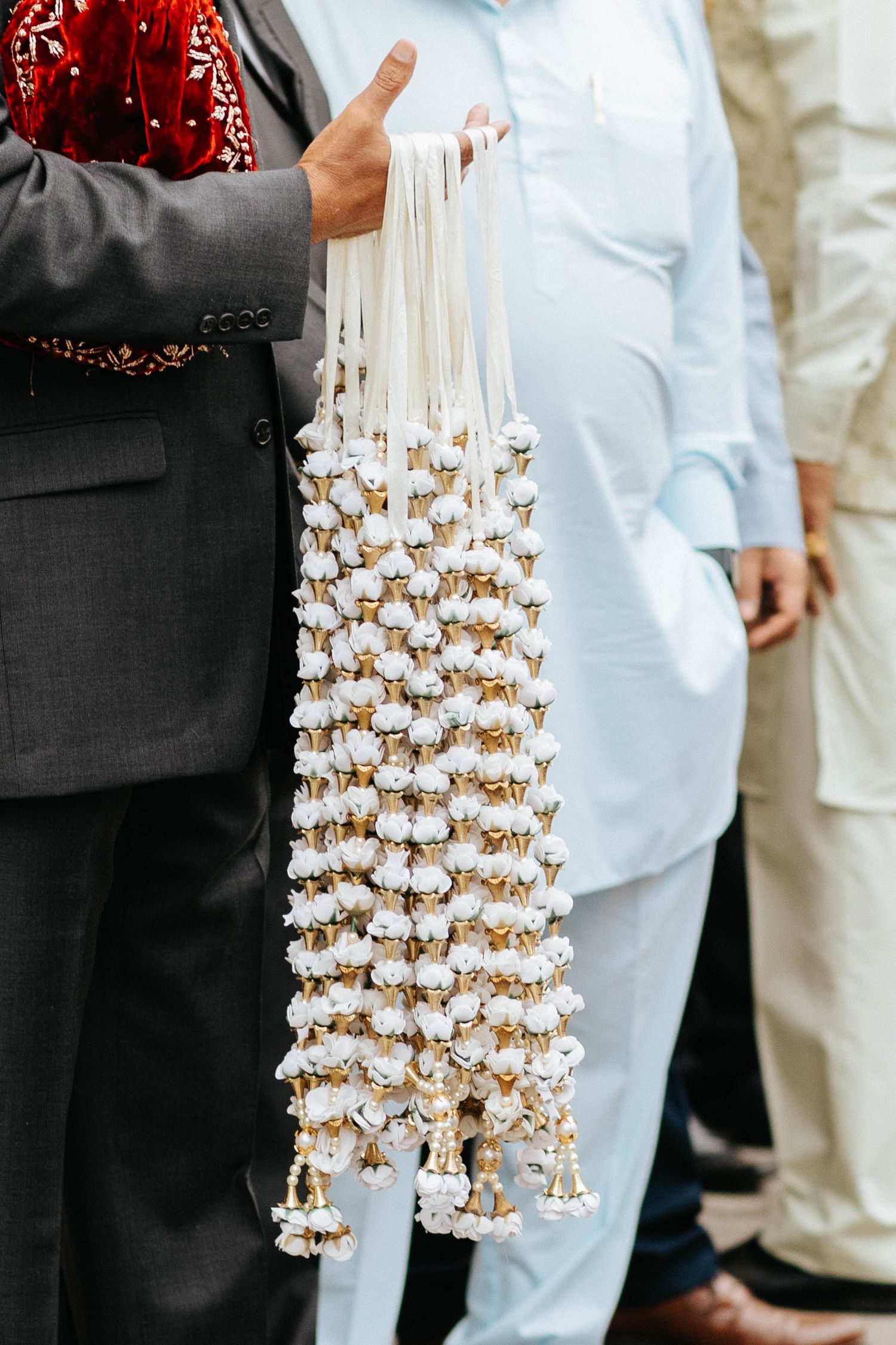 Traditional decorative garland made of small white bells and ribbons held against formal attire.