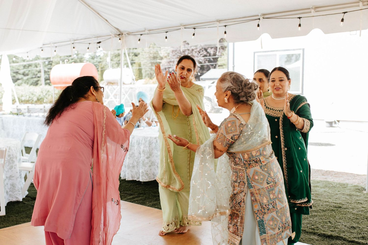 Multiple people celebrate and dance together in casual attire under a large outdoor tent at a special event.