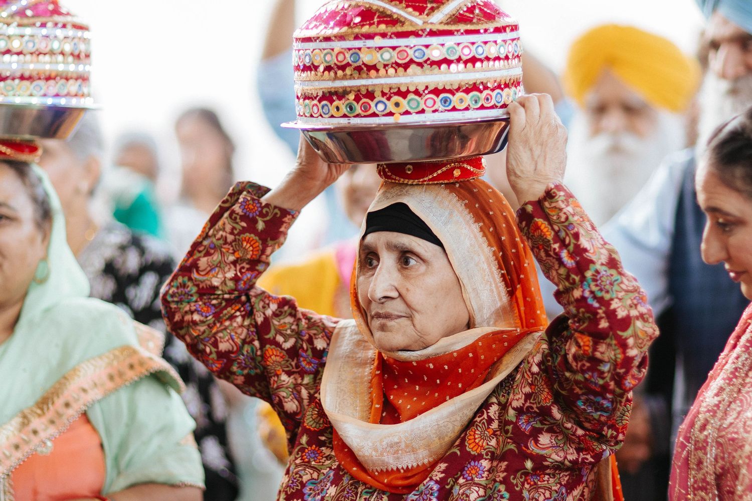 Traditional Sikh bride performs kalash ritual wearing red and gold attire during wedding ceremony.