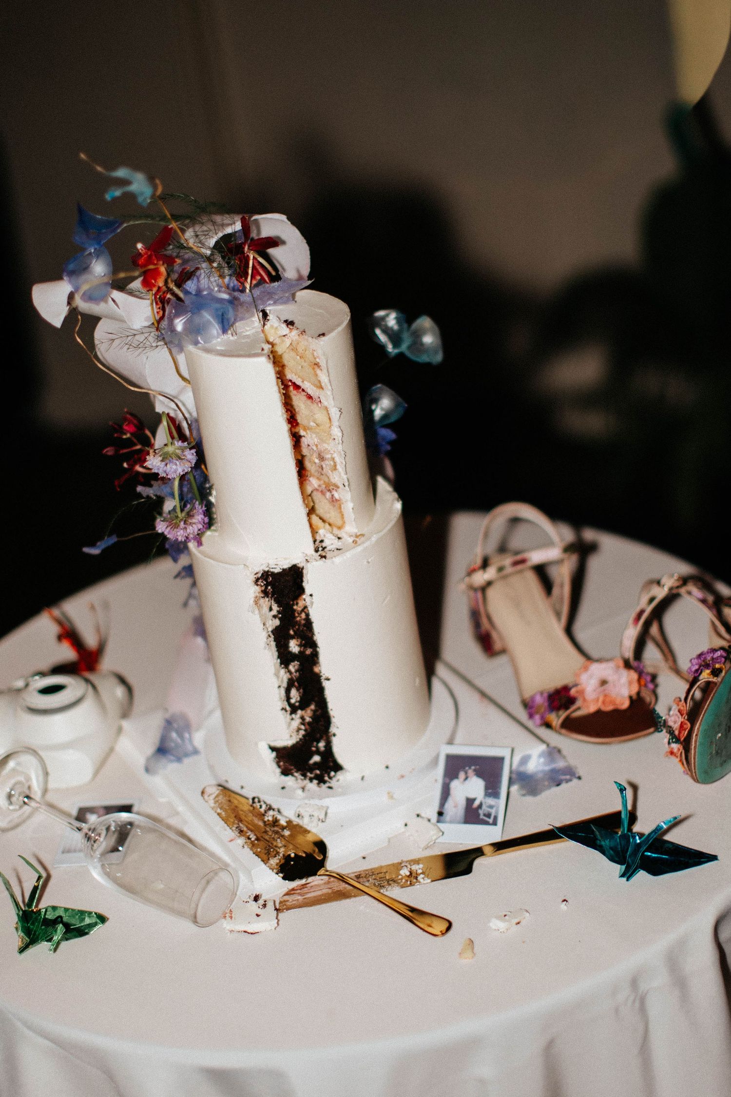 Partially cut two-tier white wedding cake with floral decorations on a table beside bridal heels.