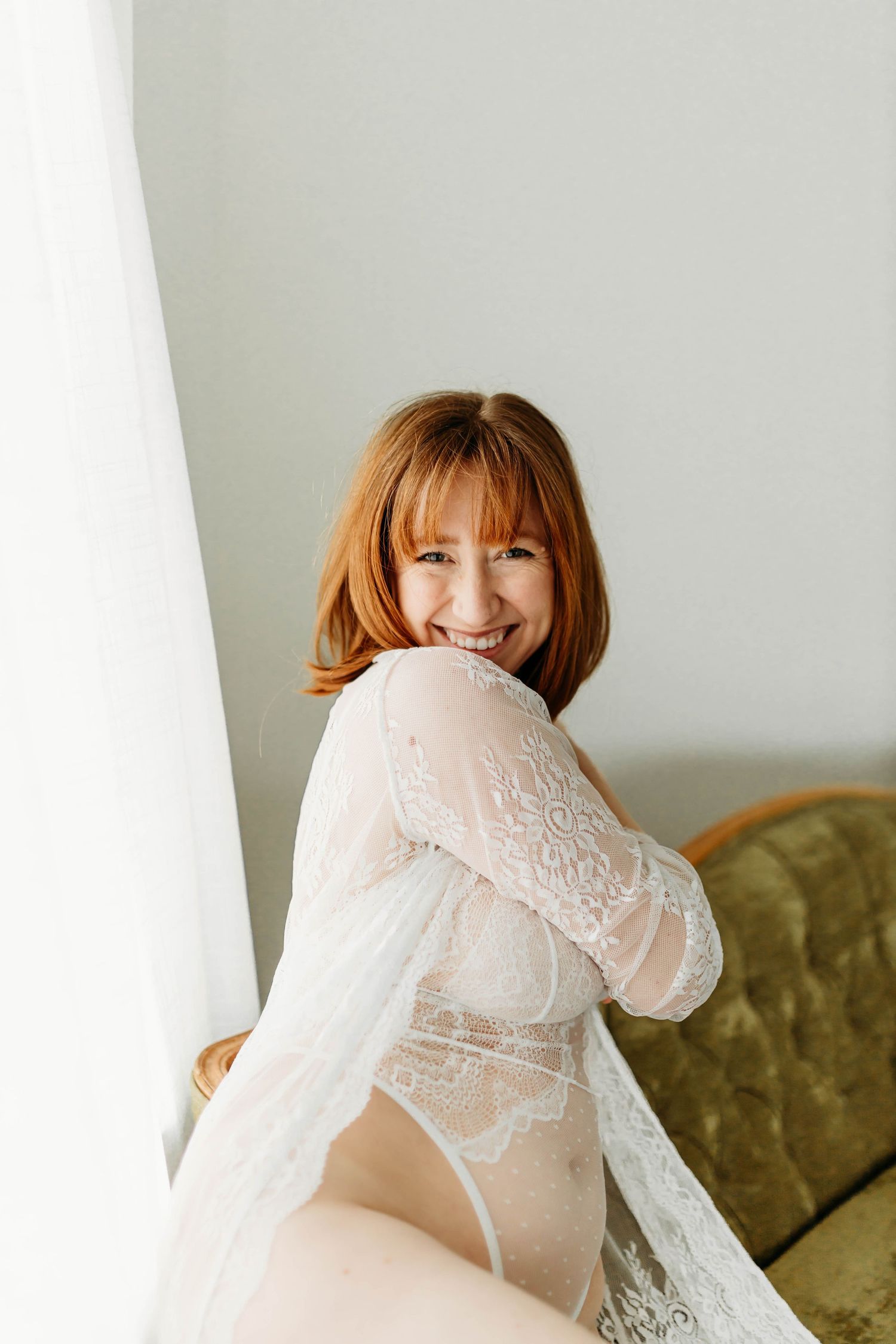Figure in delicate white lace lingerie poses playfully against green velvet couch.