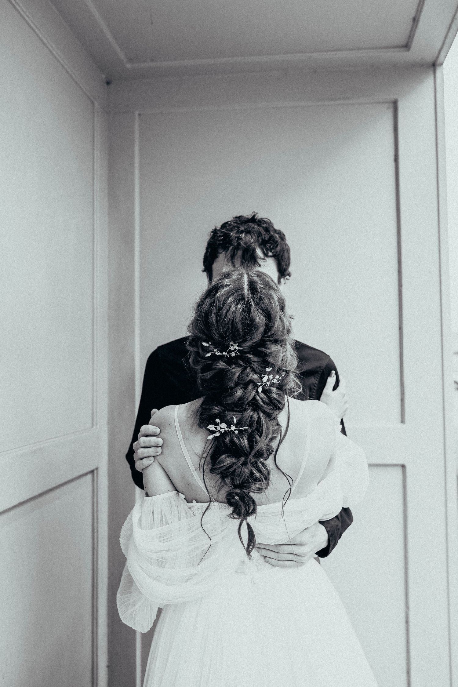 Black and white photo of an intimate wedding moment showing a couple embracing, with focus on the bride's elegant braided hairstyle.