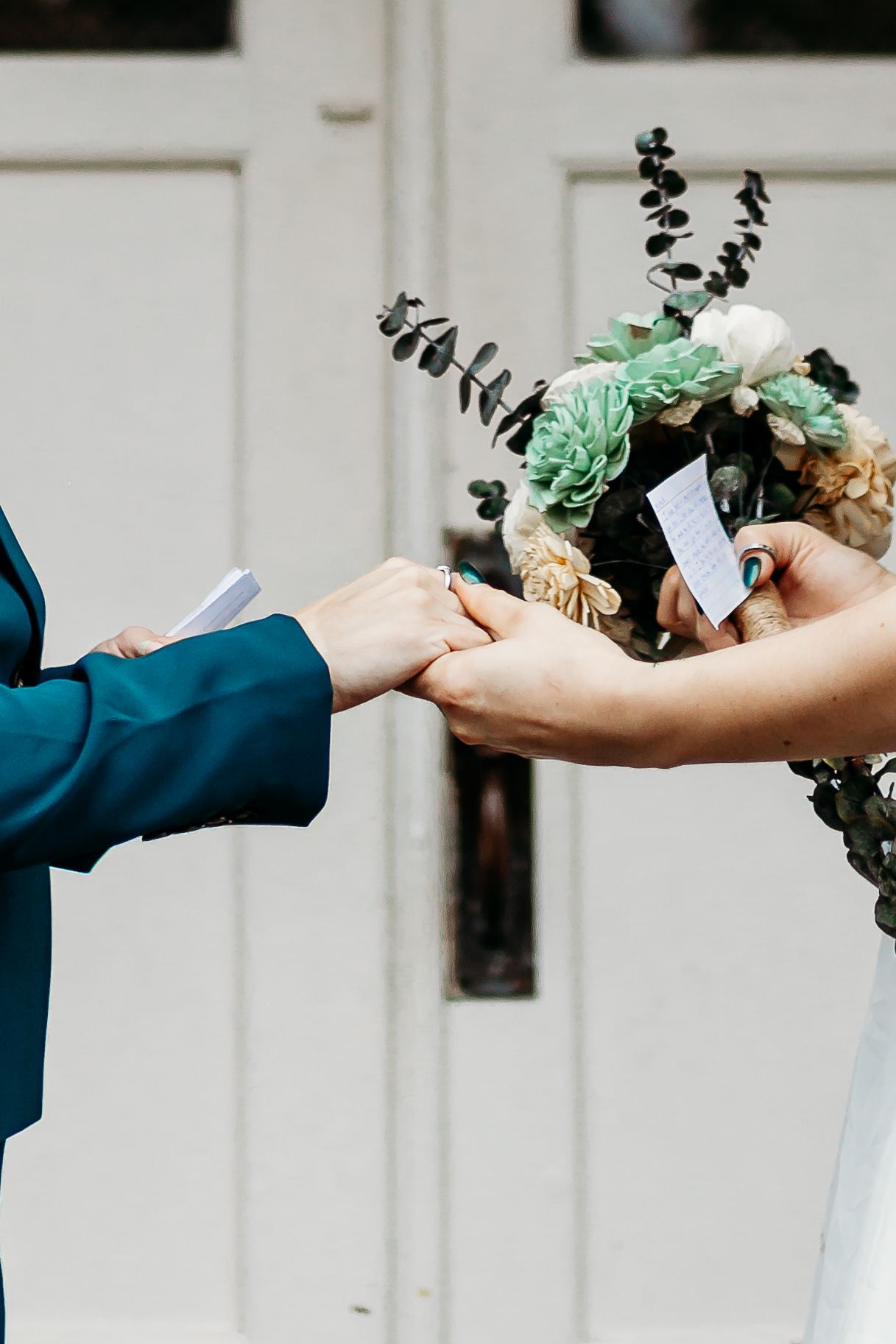Hands exchanging bouquet with mint green roses and eucalyptus against white door.
