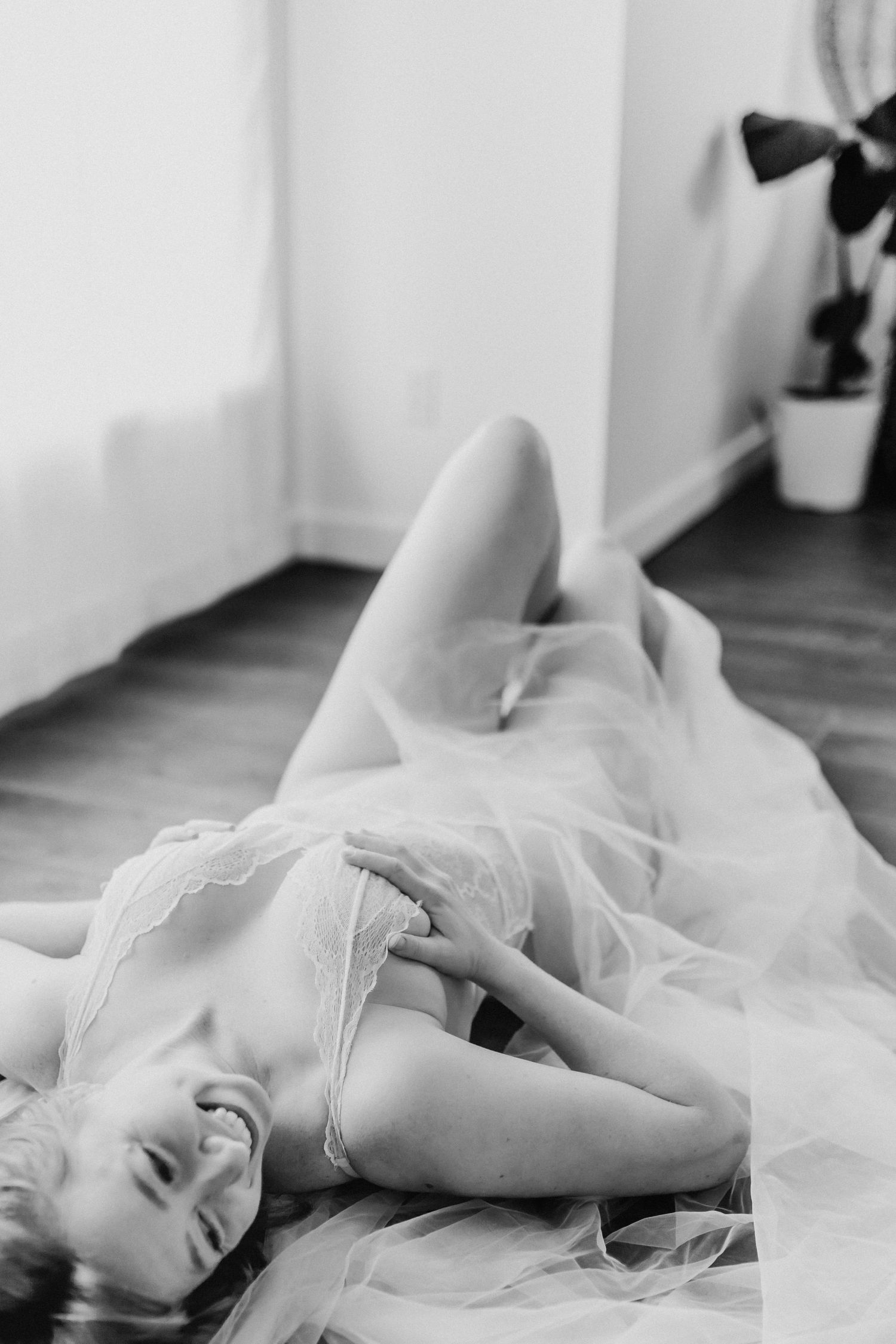 A person lies on the floor in a delicate white tulle dress in a dreamy black and white boudoir photograph.