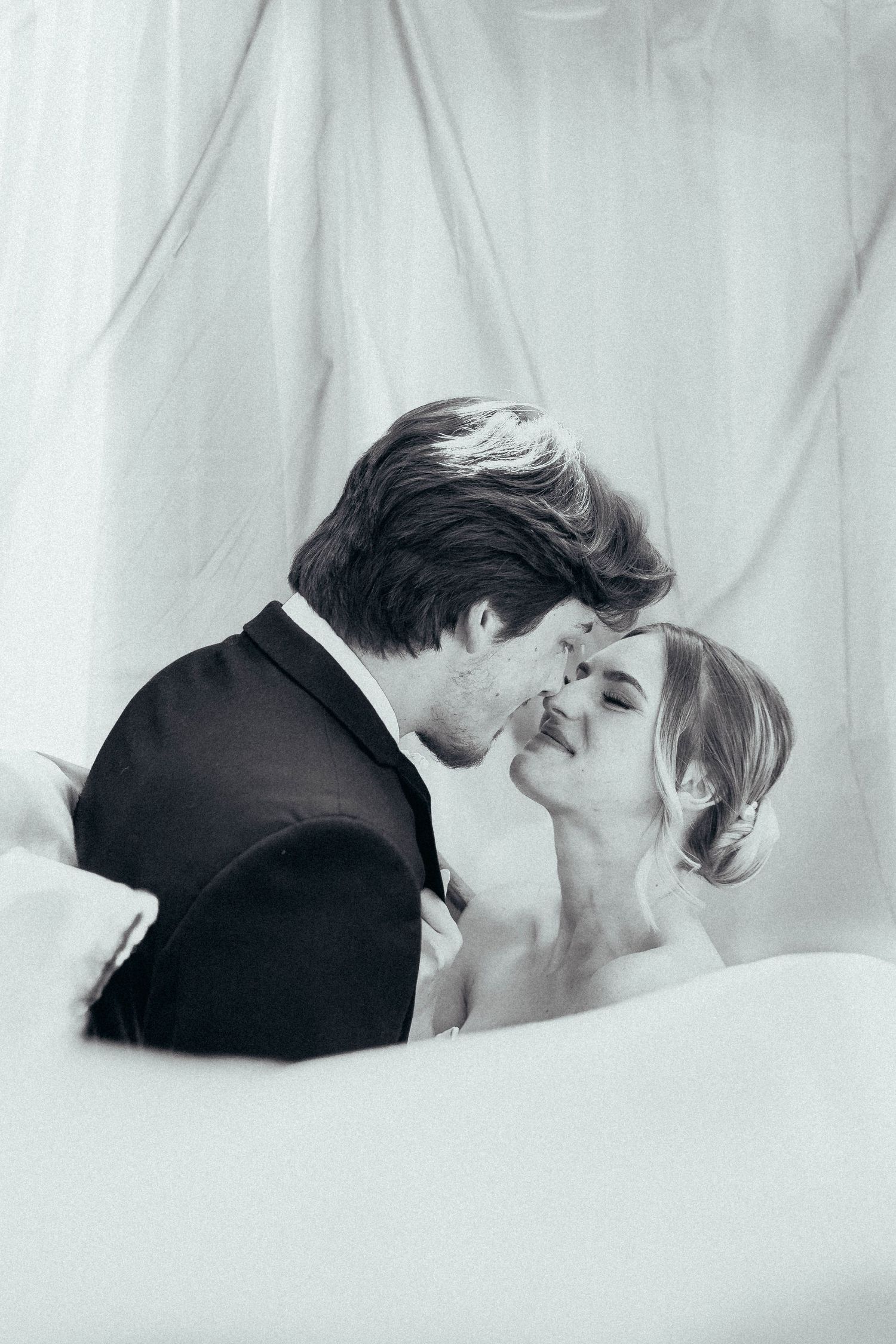 Black and white romantic portrait of bride and groom almost kissing, surrounded by soft white draping.