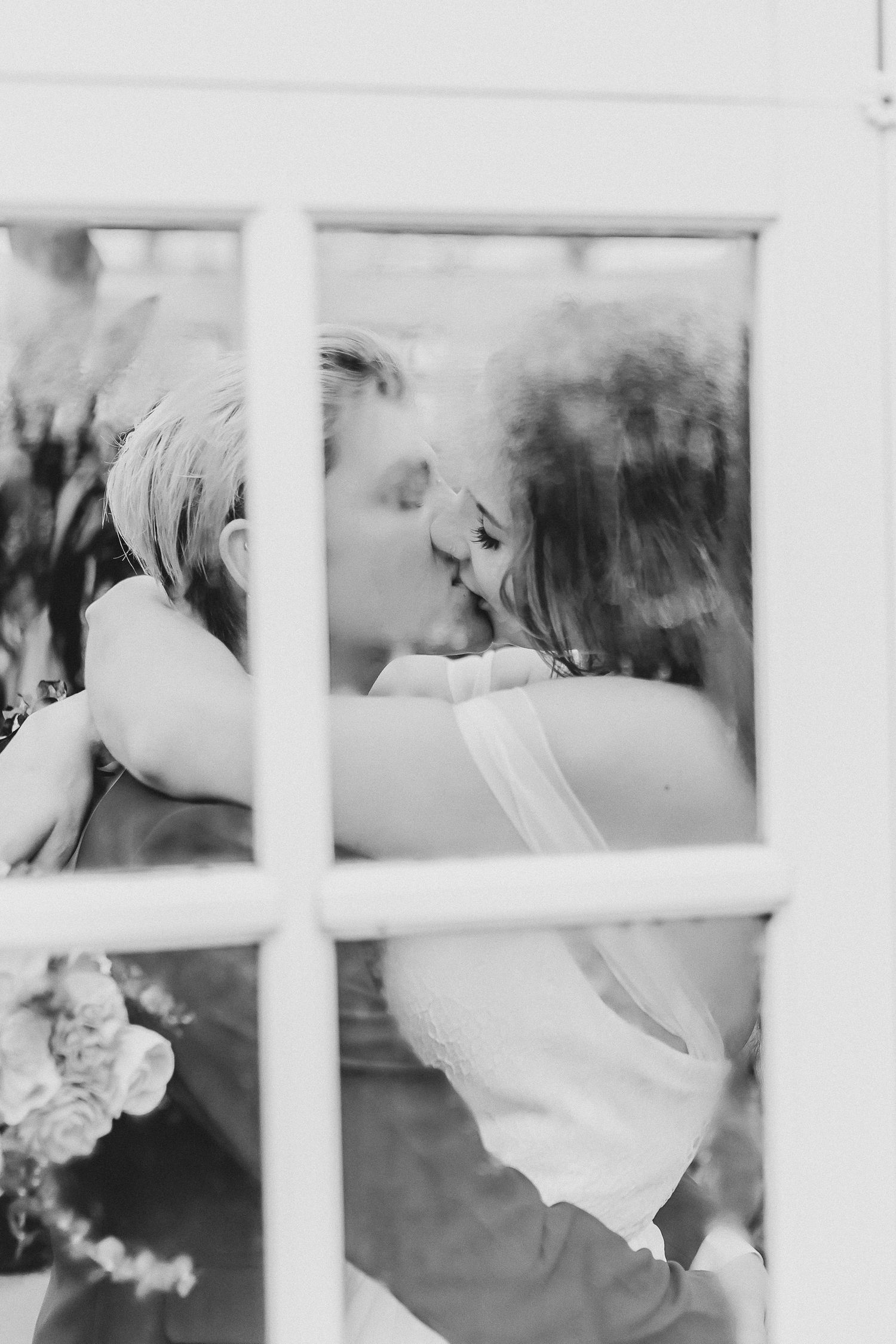 Black and white wedding photo through window panes showing tender embrace.