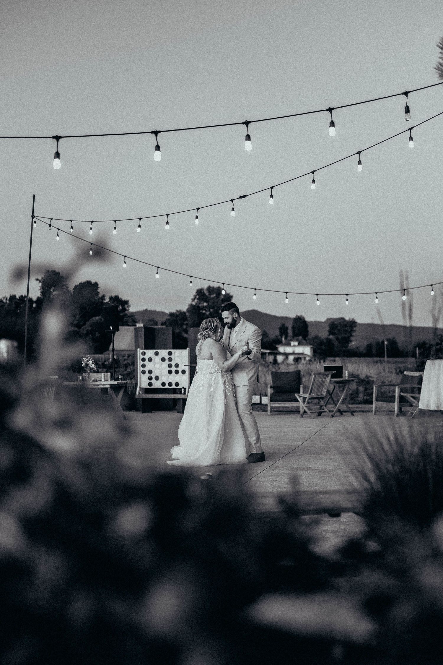 Newlyweds share romantic first dance under glowing string lights at twilight outdoor wedding reception.