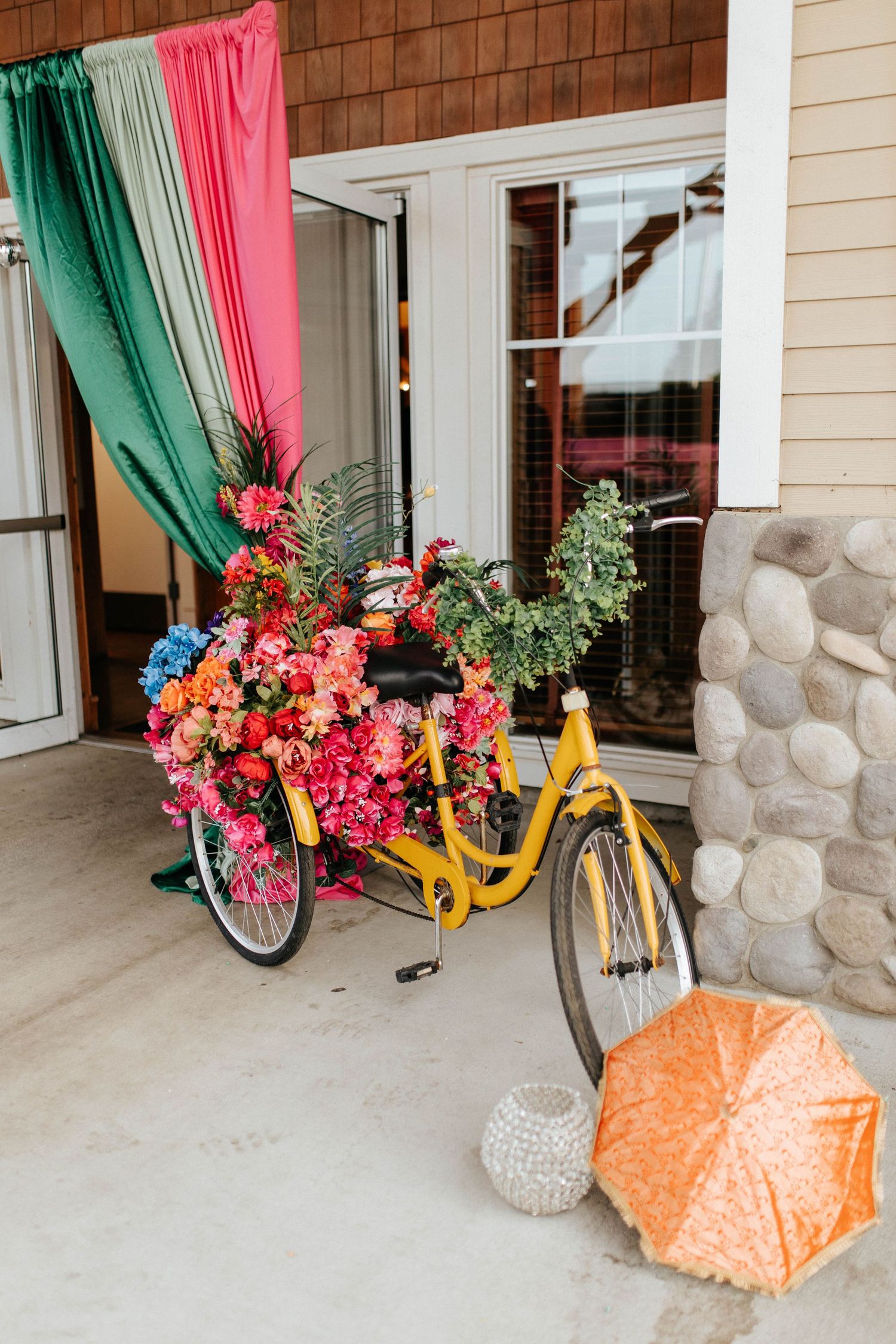Vibrant pink and teal curtains frame a doorway decorated with colorful flowers and a yellow bicycle prop.