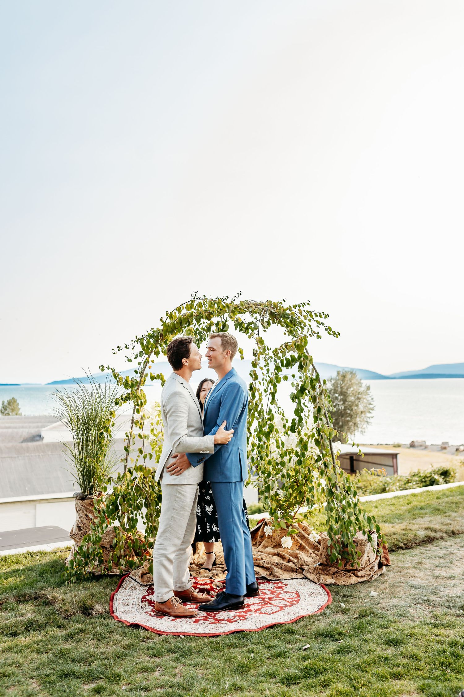 A couple shares a tender moment under a floral arch overlooking ocean views on their wedding day.