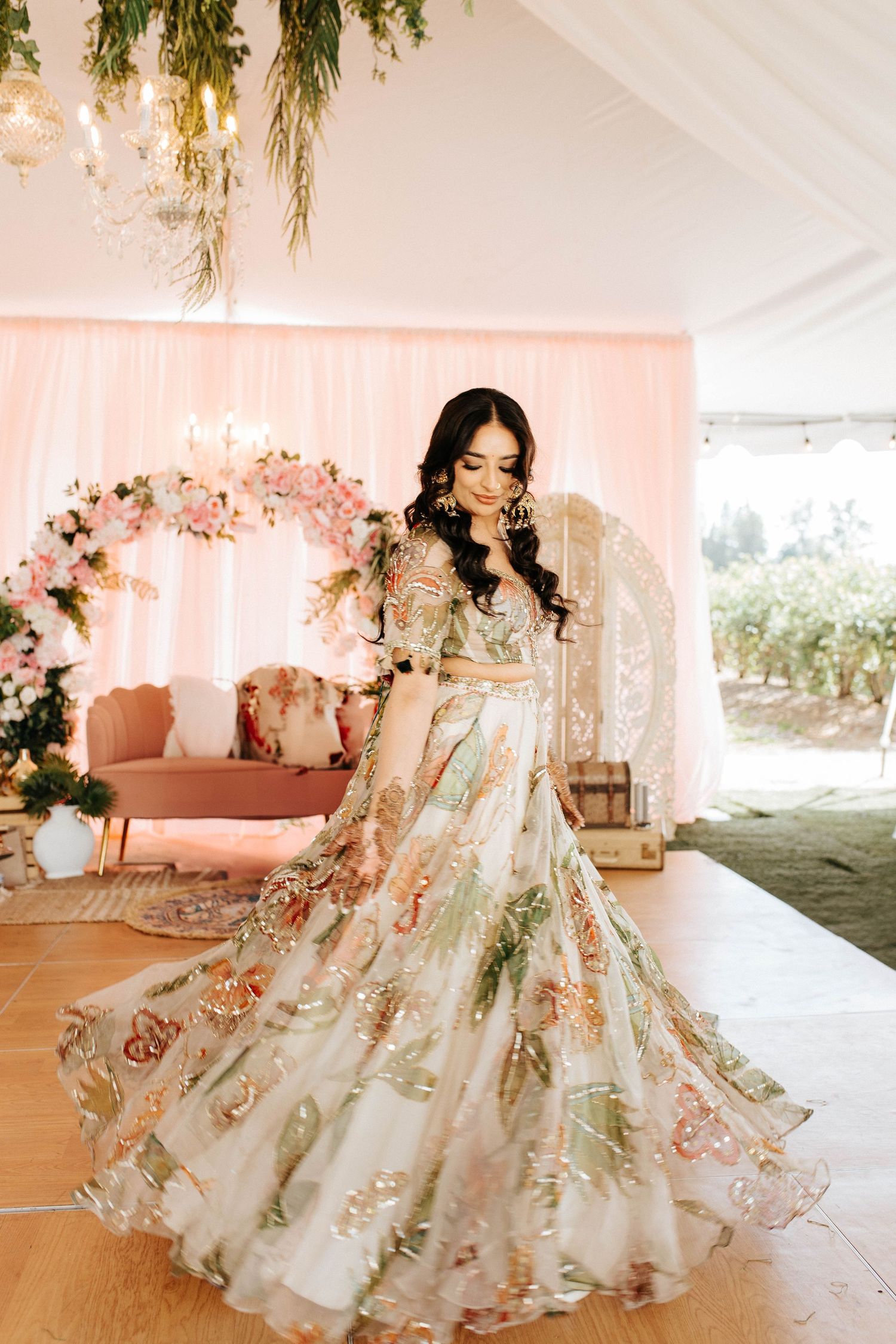 A stunning floral wedding lehenga with intricate embroidery twirls in a pink-decorated venue setting.