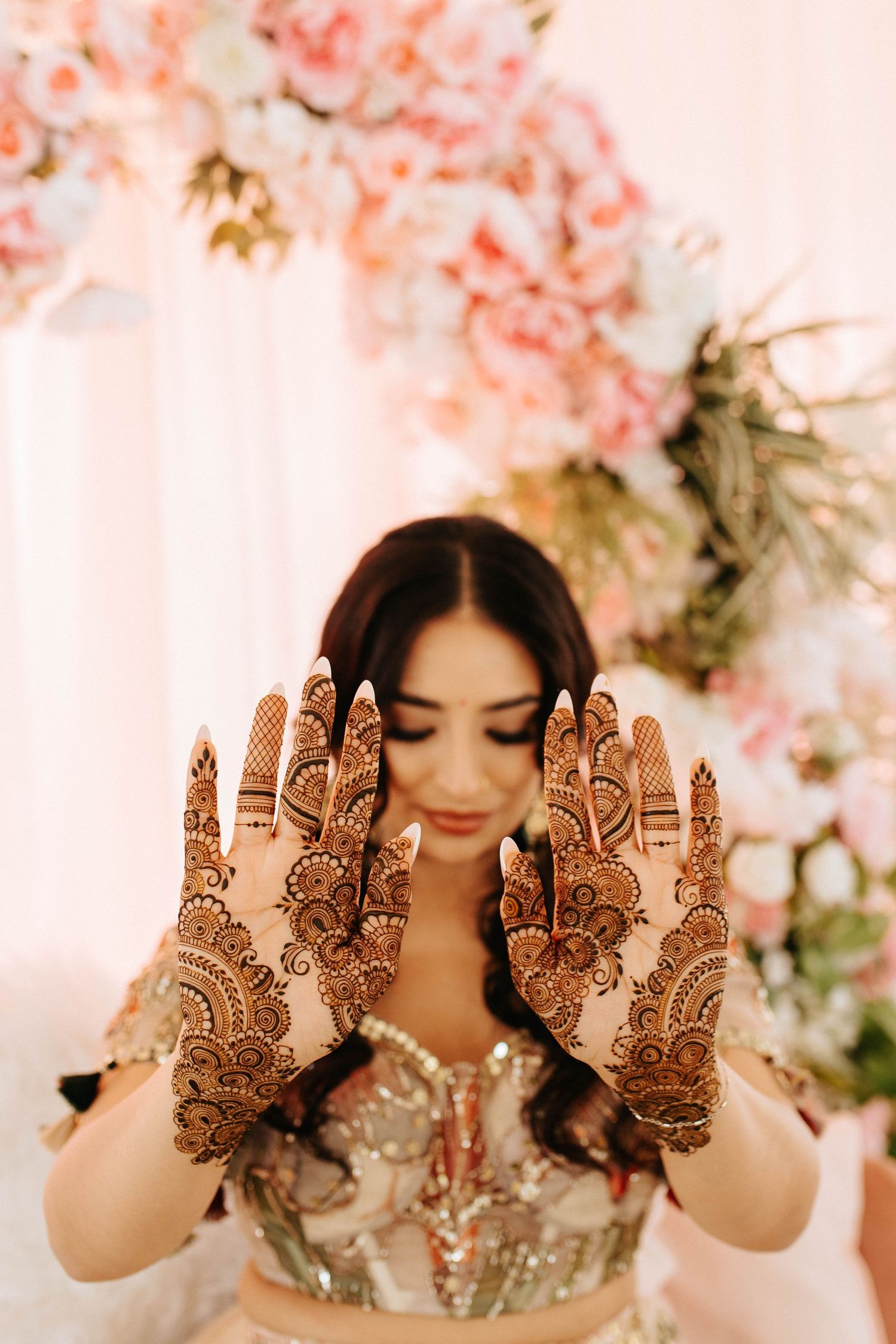 Ornate henna designs displayed on both palms against a backdrop of soft pink cherry blossoms.