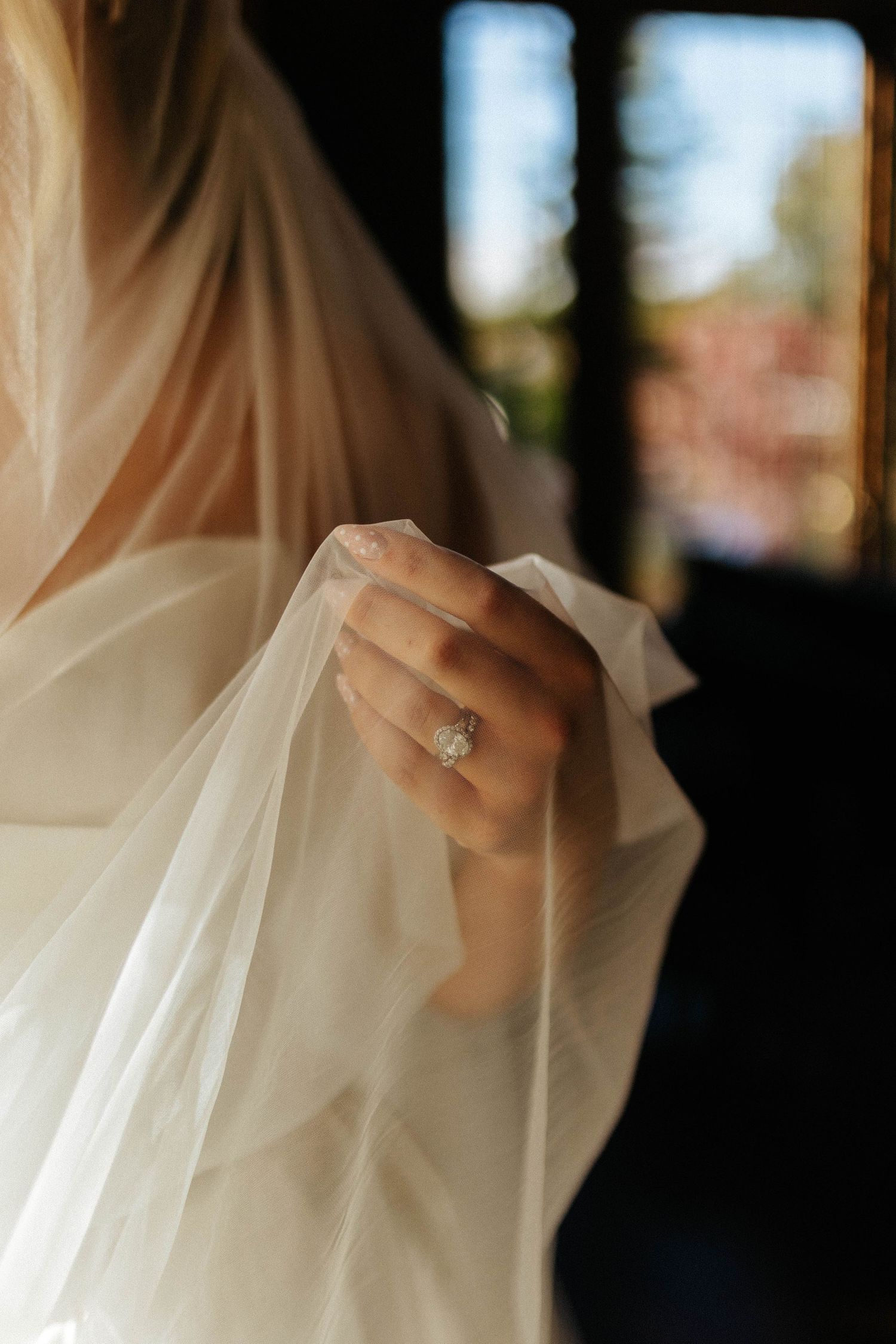 Close-up of bride's hand holding a sheer veil, showcasing a sparkling diamond engagement ring.